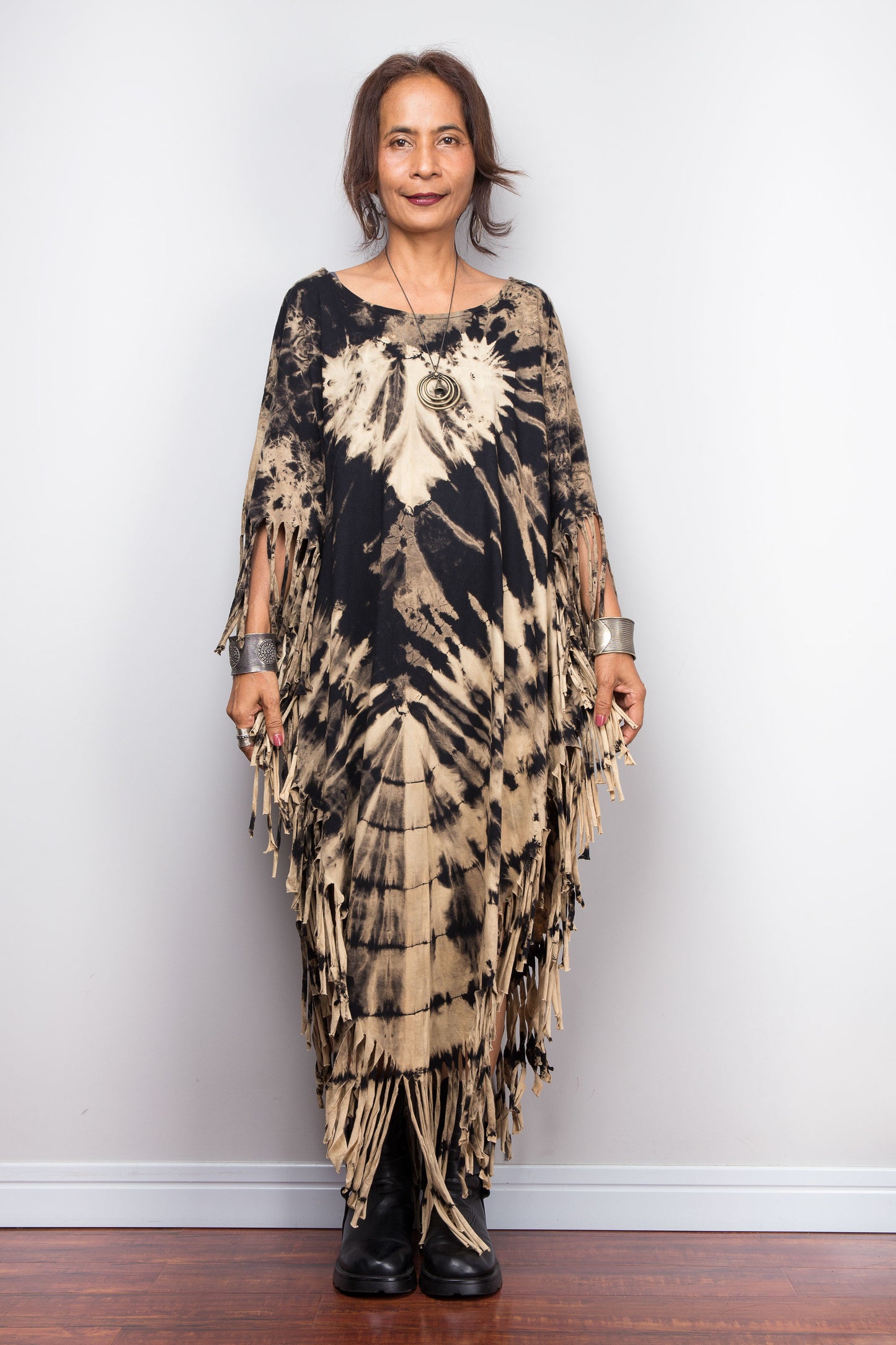 Petite Woman wearing a unique Nuichan brand, reverse tie dye poncho tunic with fringes against a plain background