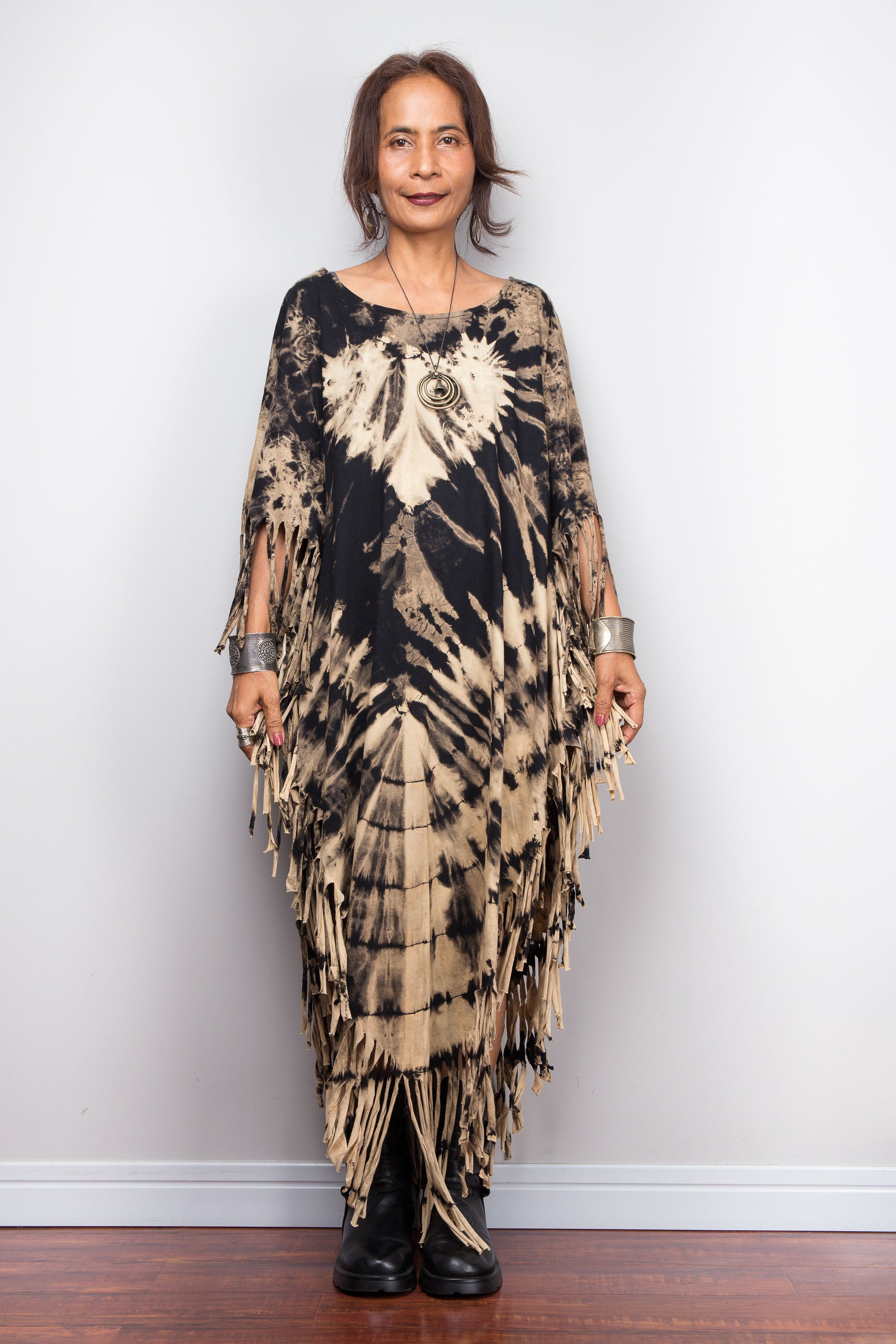 Petite Woman wearing a unique Nuichan brand, reverse tie dye poncho tunic with fringes against a plain background