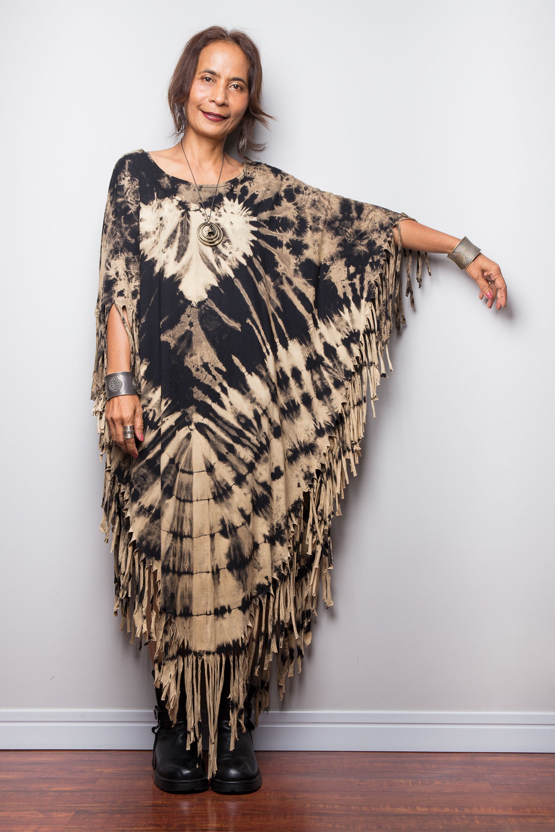 Petite Woman wearing a unique Nuichan brand, reverse tie dye poncho top with fringes against a plain background