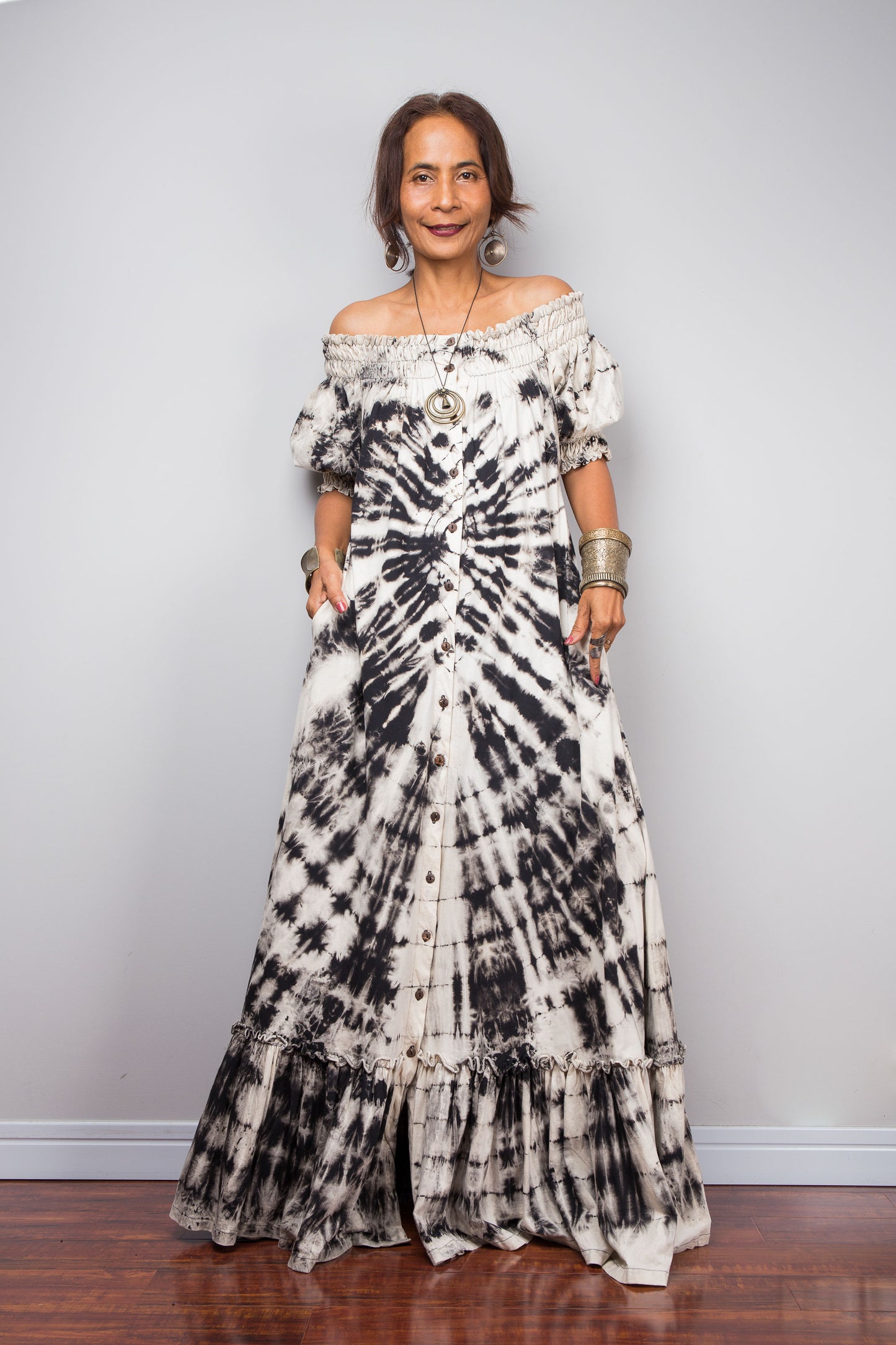 Front view of a model styling the Nuichan reverse tie-dye maxi dress off-the-shoulder, showcasing the smocked bodice and dramatic monochrome spiral pattern.