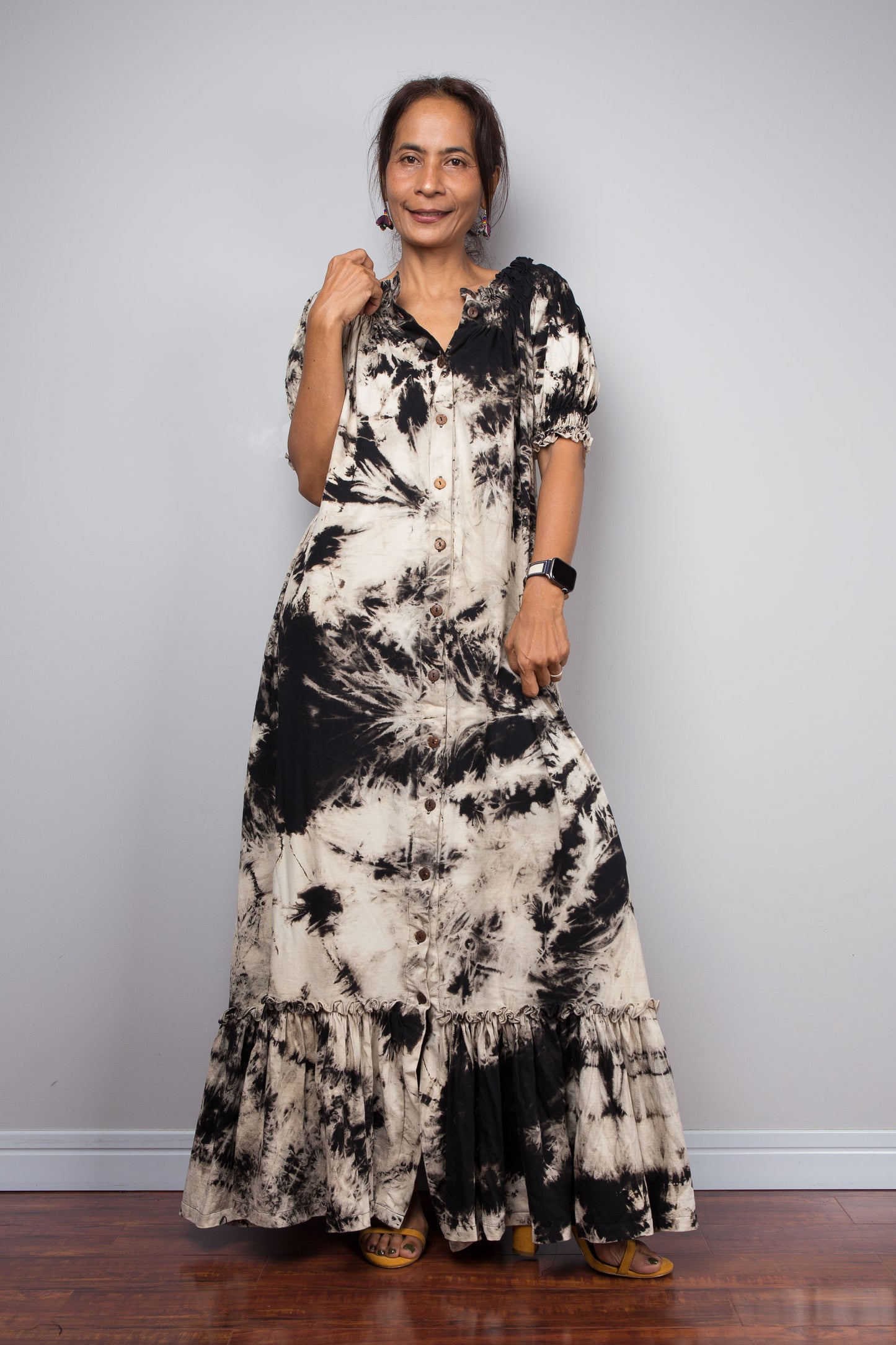 Front view of a model wearing the Nuichan reverse tie dye maxi shirt dress with buttons partially undone at the hem, demonstrating the adjustable walking slit detail and the sweeping tiered ruffle hem in motion