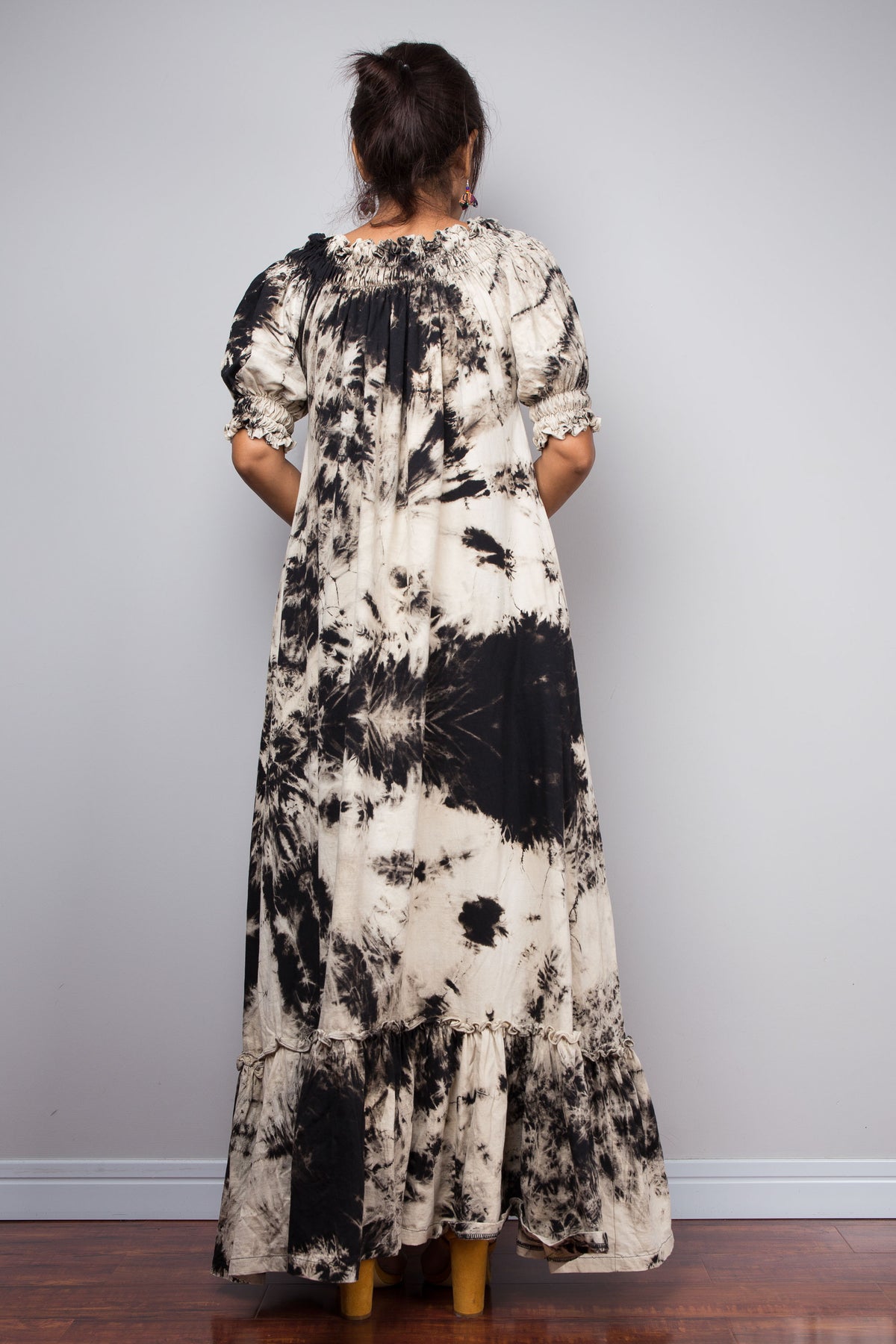 Rear view of a model in the Nuichan off-the-shoulder reverse tie dye maxi dress, showing the full floor-length silhouette, ruffled sleeve detail at the shoulders, and the continuation of the high-contrast reverse tie dye pattern across the back