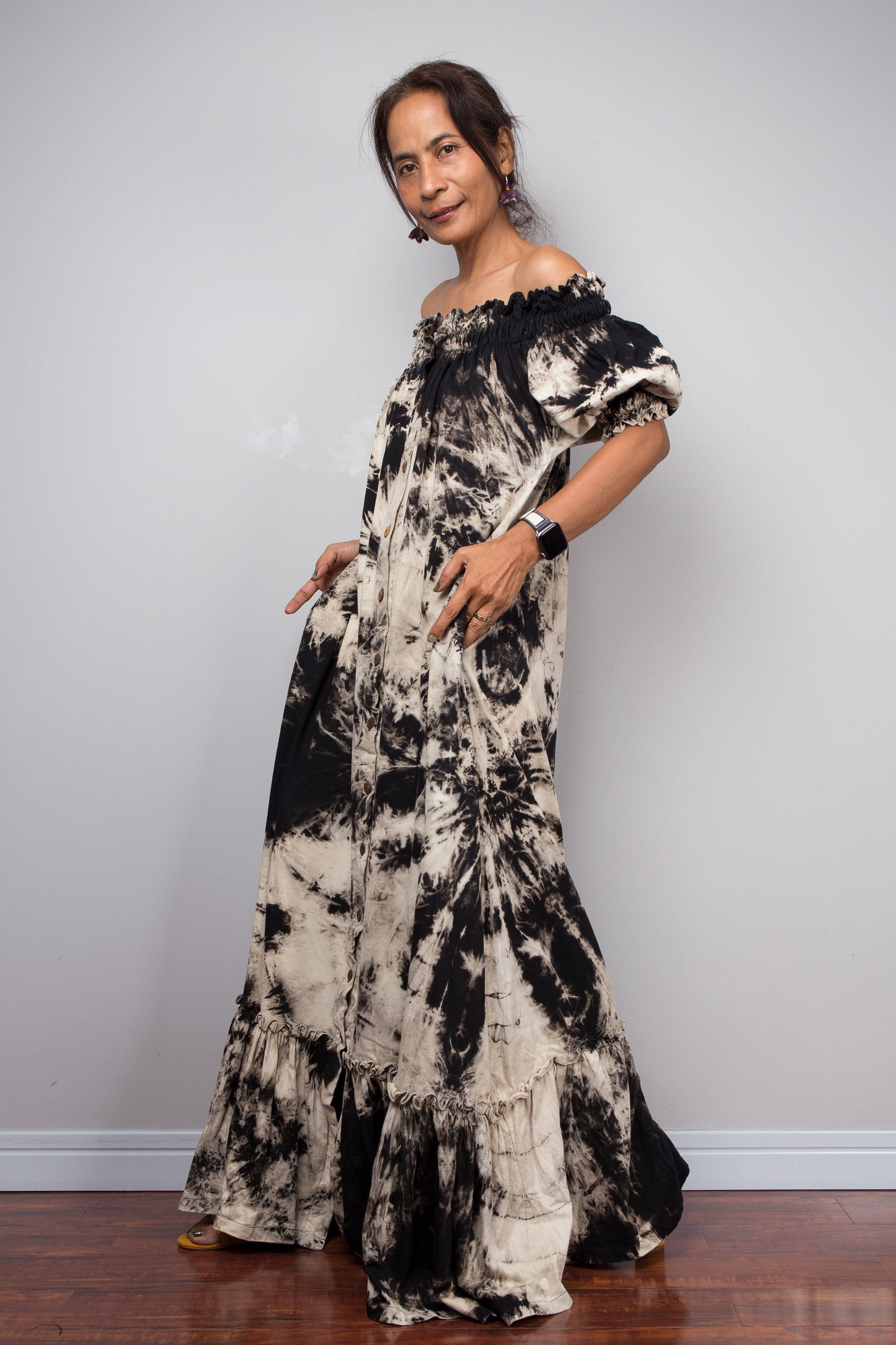 Full-length side view of a model in the Nuichan reverse tie dye off-shoulder button-down maxi dress, showcasing the complete silhouette from elasticated smocked neckline to tiered ruffle hem with deep side pockets