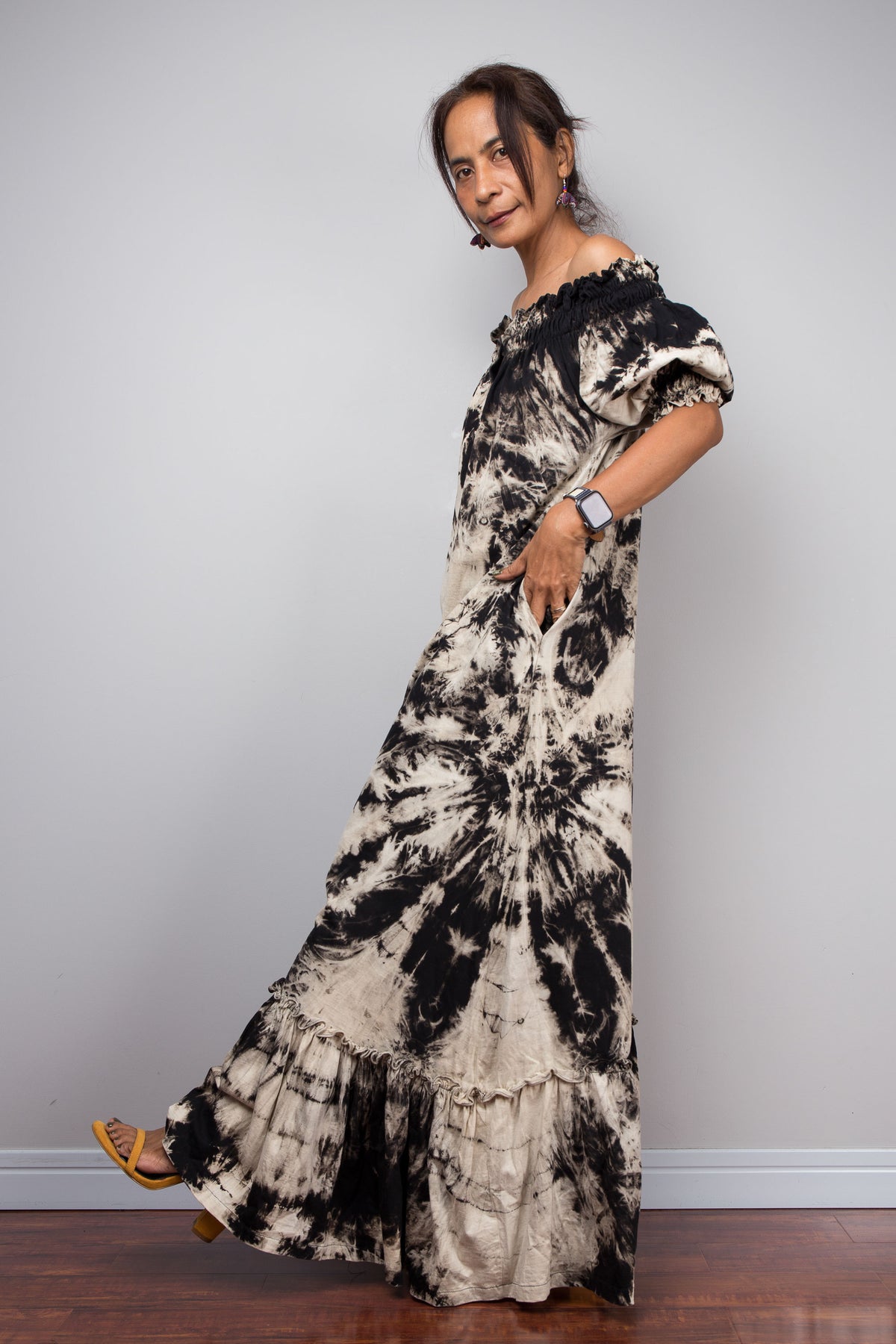 Full-length side view of a model in the Nuichan reverse tie dye off-shoulder button-down maxi dress, showcasing the complete silhouette from elasticated smocked neckline to tiered ruffle hem with deep side pockets