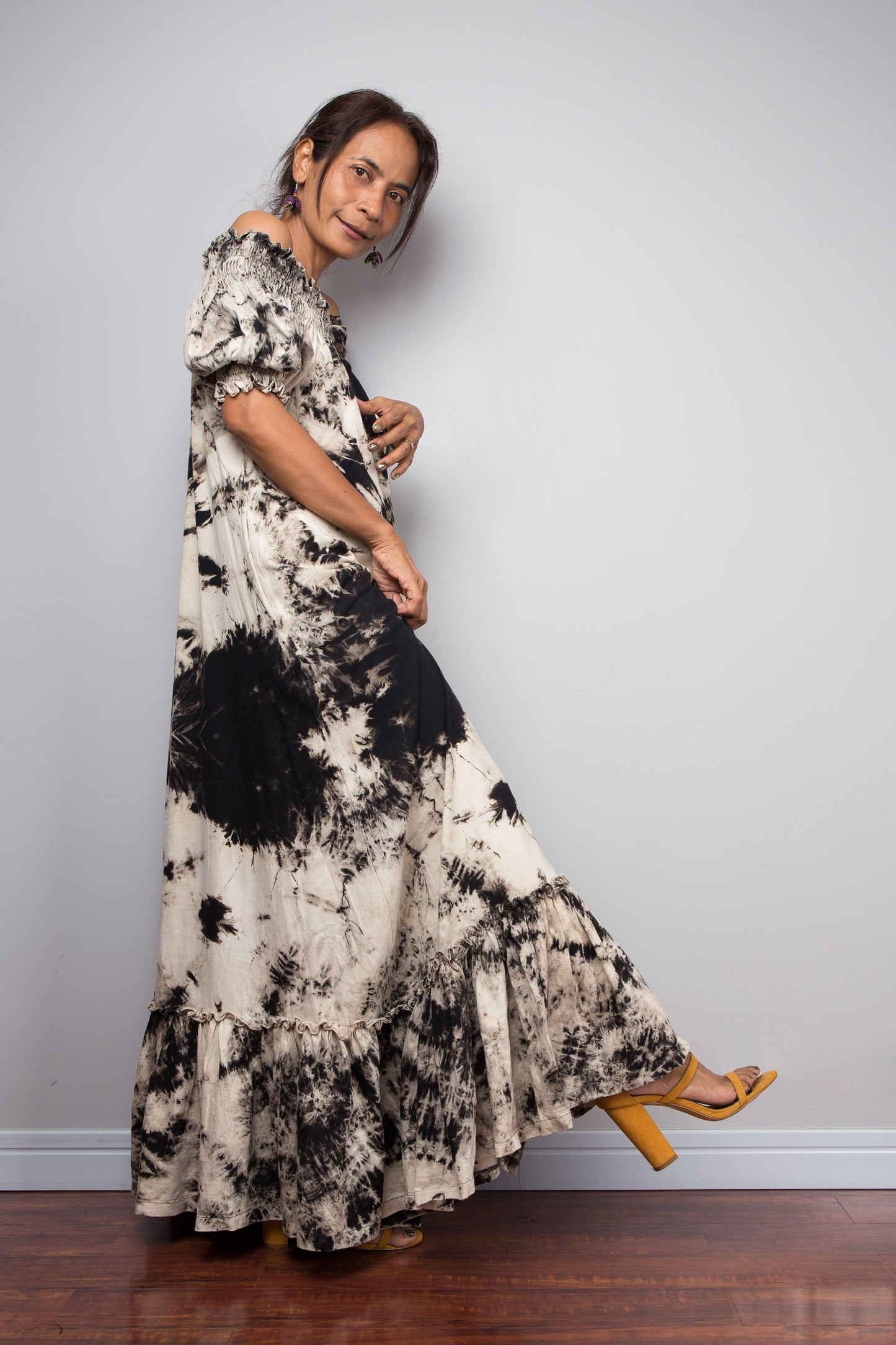 Full-length side view of a petite model in the Nuichan reverse tie dye off-shoulder button-down maxi dress, showcasing the complete silhouette from elasticated smocked neckline to tiered ruffle hem with deep side pockets
