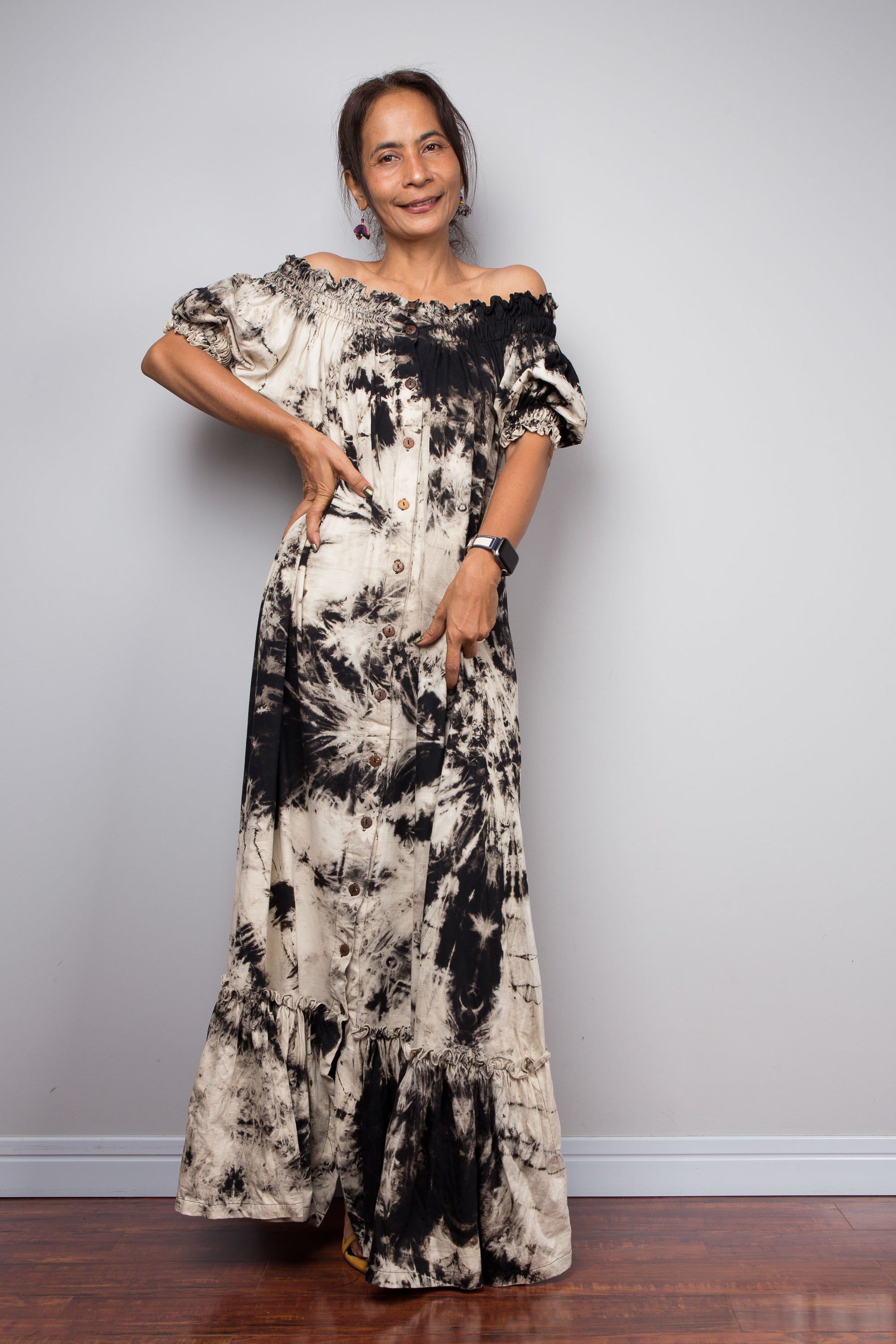 Front view of a model wearing the Nuichan reverse tie dye maxi shirt dress with the smocked neckline pulled down off the shoulders, highlighting the romantic bohemian off-shoulder styling and hand-dyed black and sand earth fade pattern