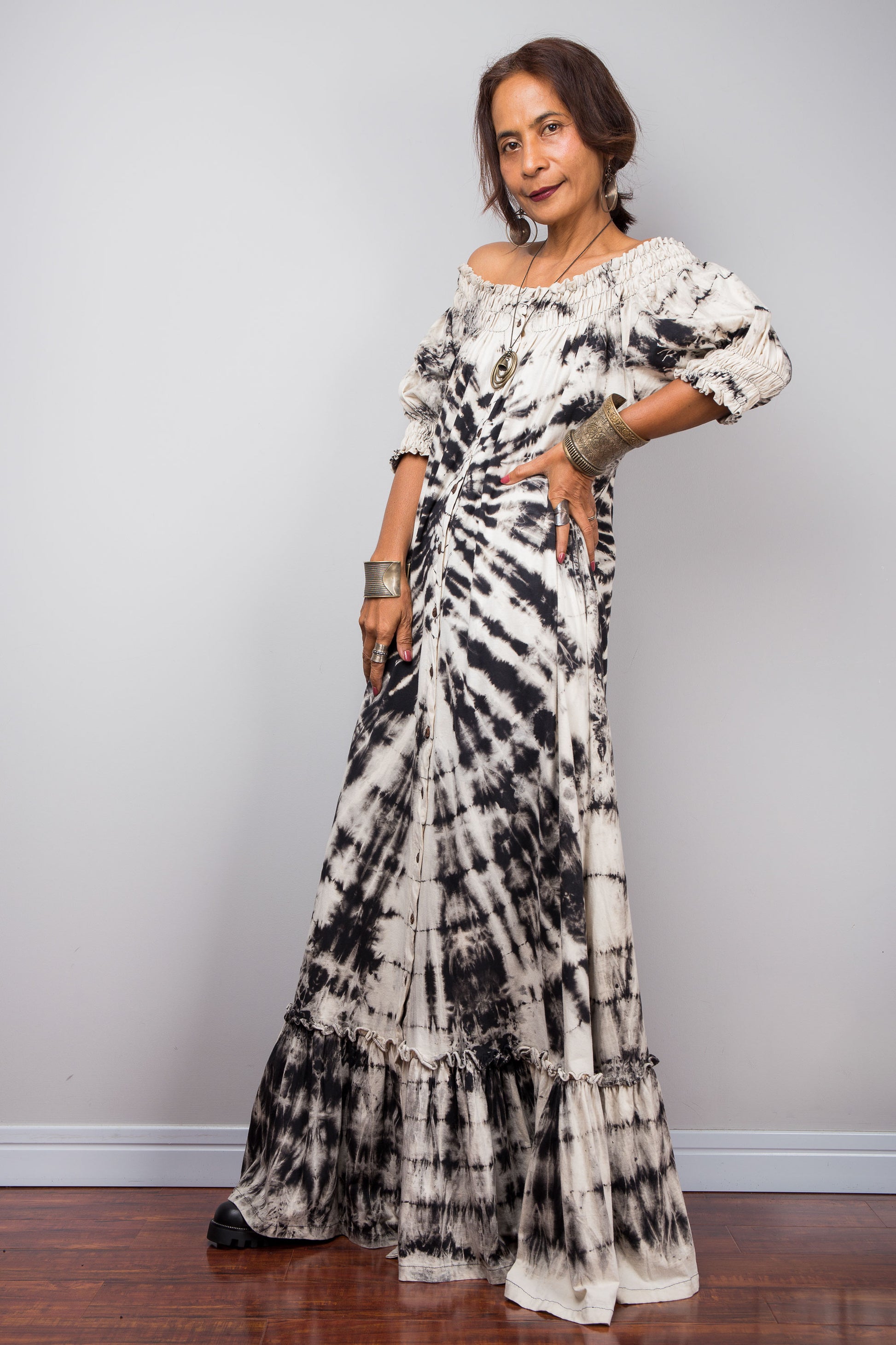 Front side view of a model styling the Nuichan reverse tie-dye maxi dress off-the-shoulder, showcasing the smocked bodice and dramatic monochrome spiral pattern.