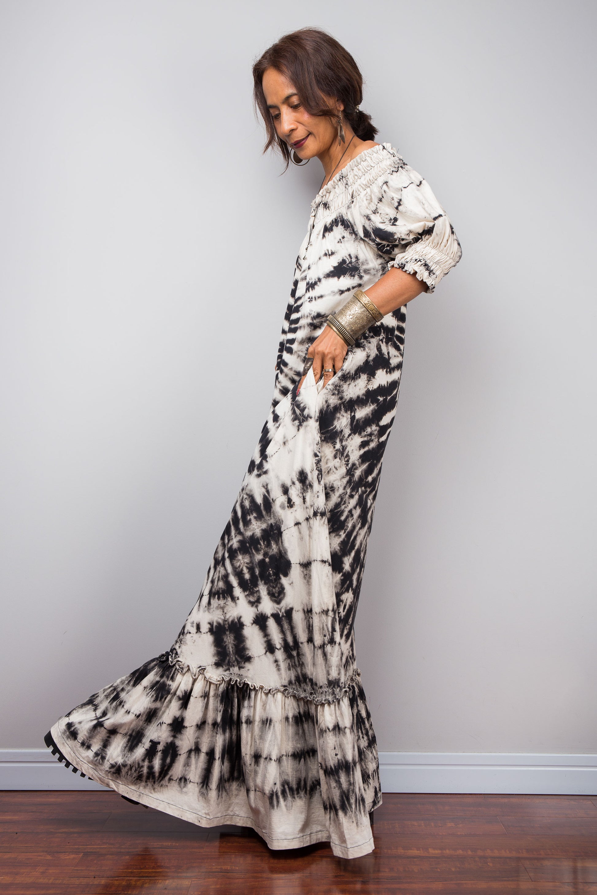 Full side view of a model styling the Nuichan reverse tie-dye maxi dress off-the-shoulder, showcasing the smocked bodice and dramatic monochrome spiral pattern.