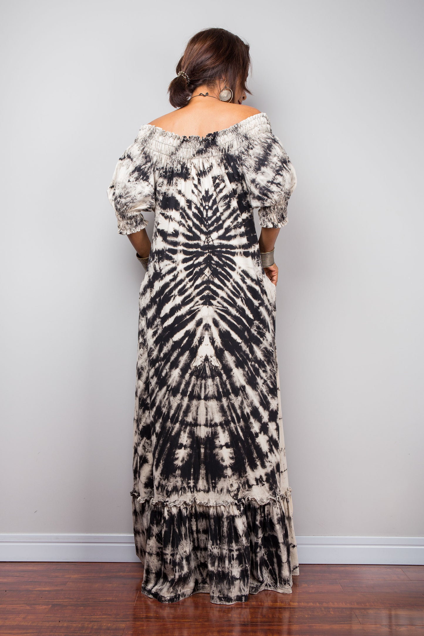 Back view of a model styling the Nuichan reverse tie-dye maxi dress off-the-shoulder, showcasing the smocked bodice and dramatic monochrome spiral pattern.
