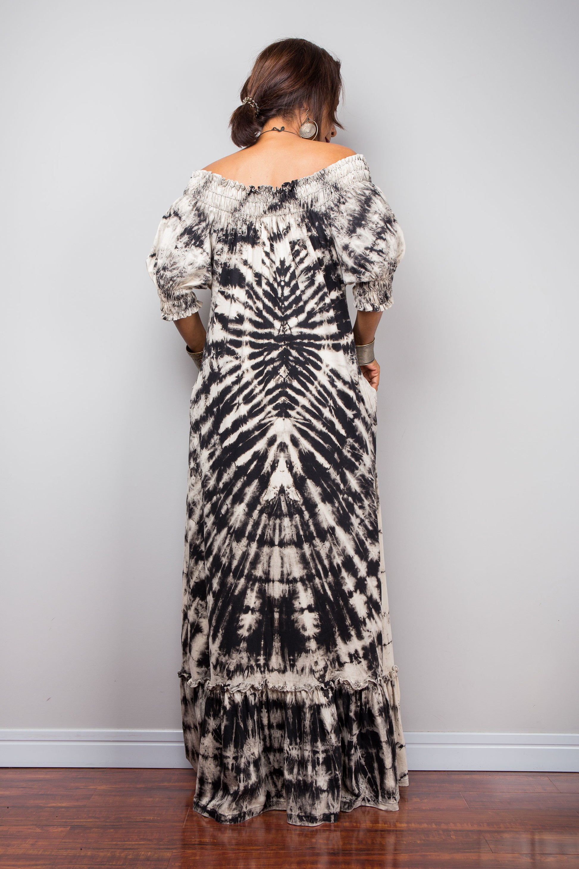 Back view of a model styling the Nuichan reverse tie-dye maxi dress off-the-shoulder, showcasing the smocked bodice and dramatic monochrome spiral pattern.