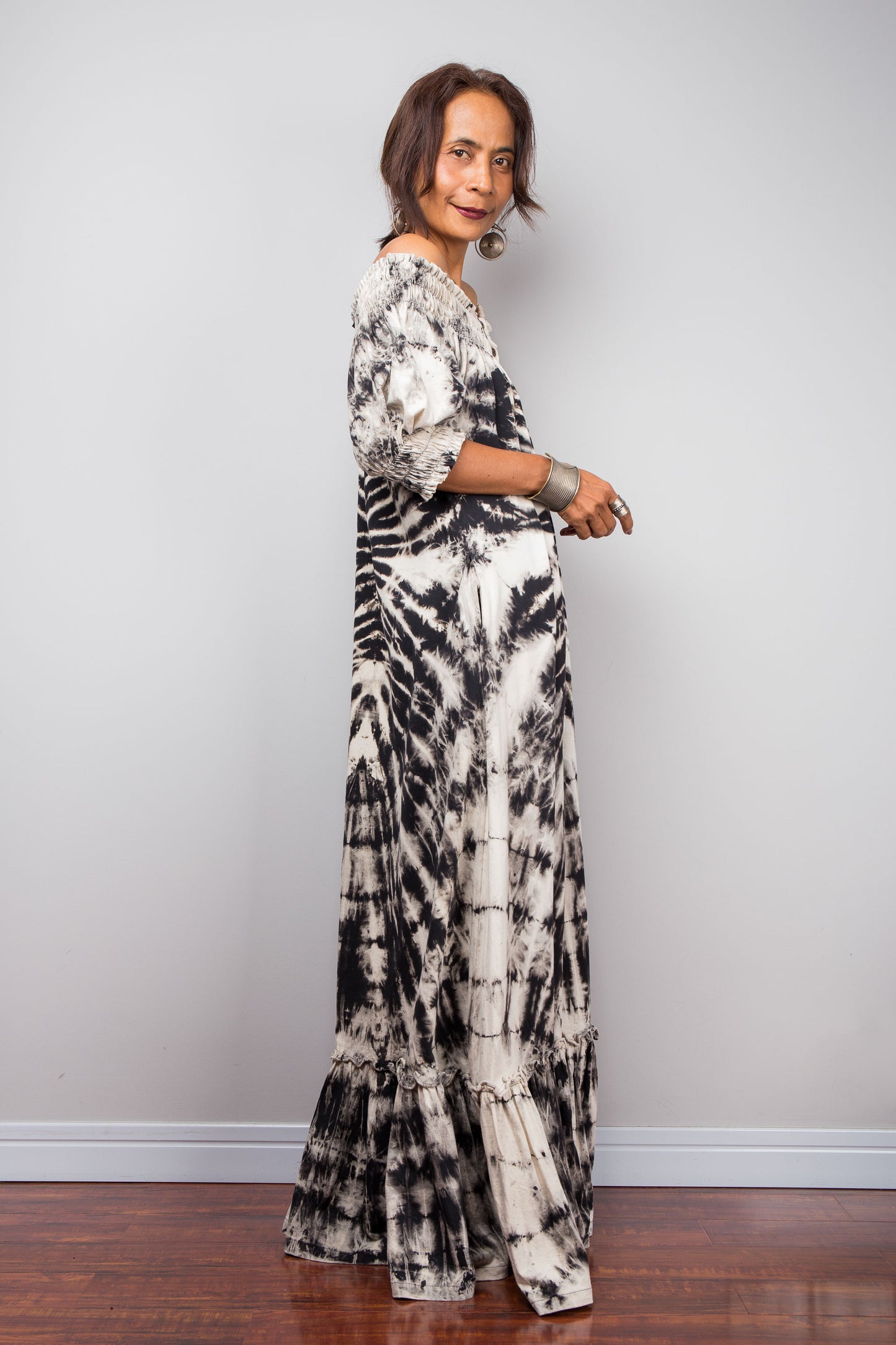Full on side view of a model styling the Nuichan reverse tie-dye maxi dress off-the-shoulder, showcasing the smocked bodice and dramatic monochrome spiral pattern.
