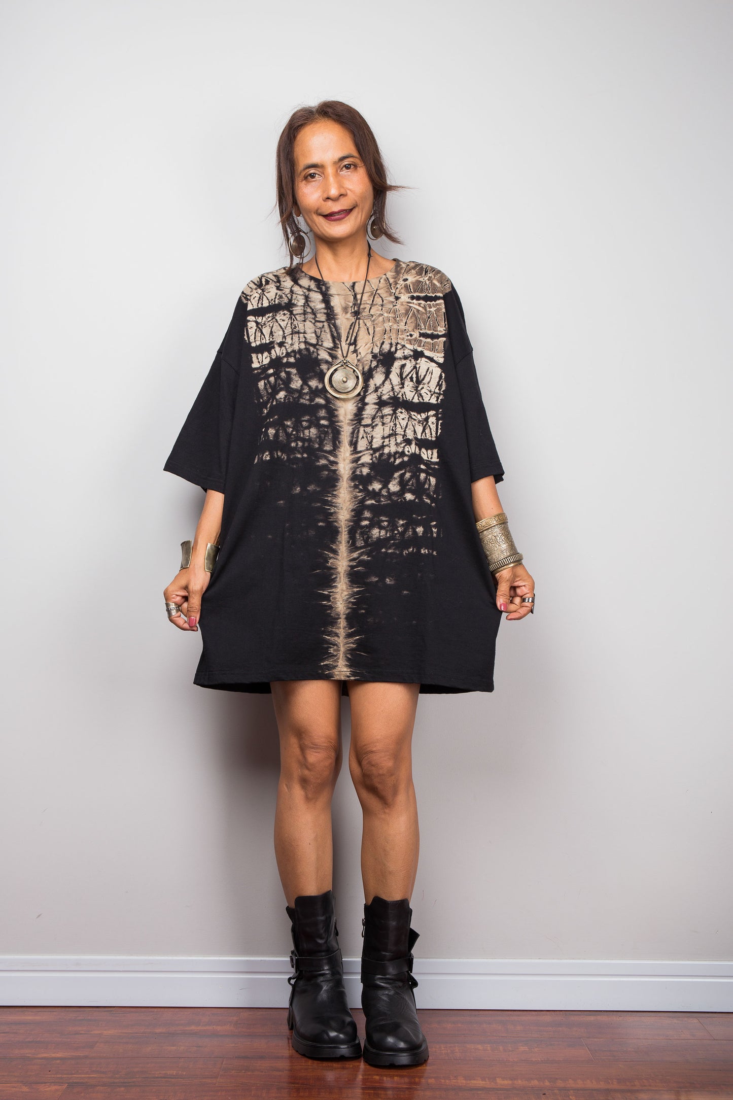 Front view of a petite woman styling Nuichan's oversized reverse tie-dye t-shirt dress with black boots, showcasing the loose boxy fit and vertical sand-colored starburst pattern