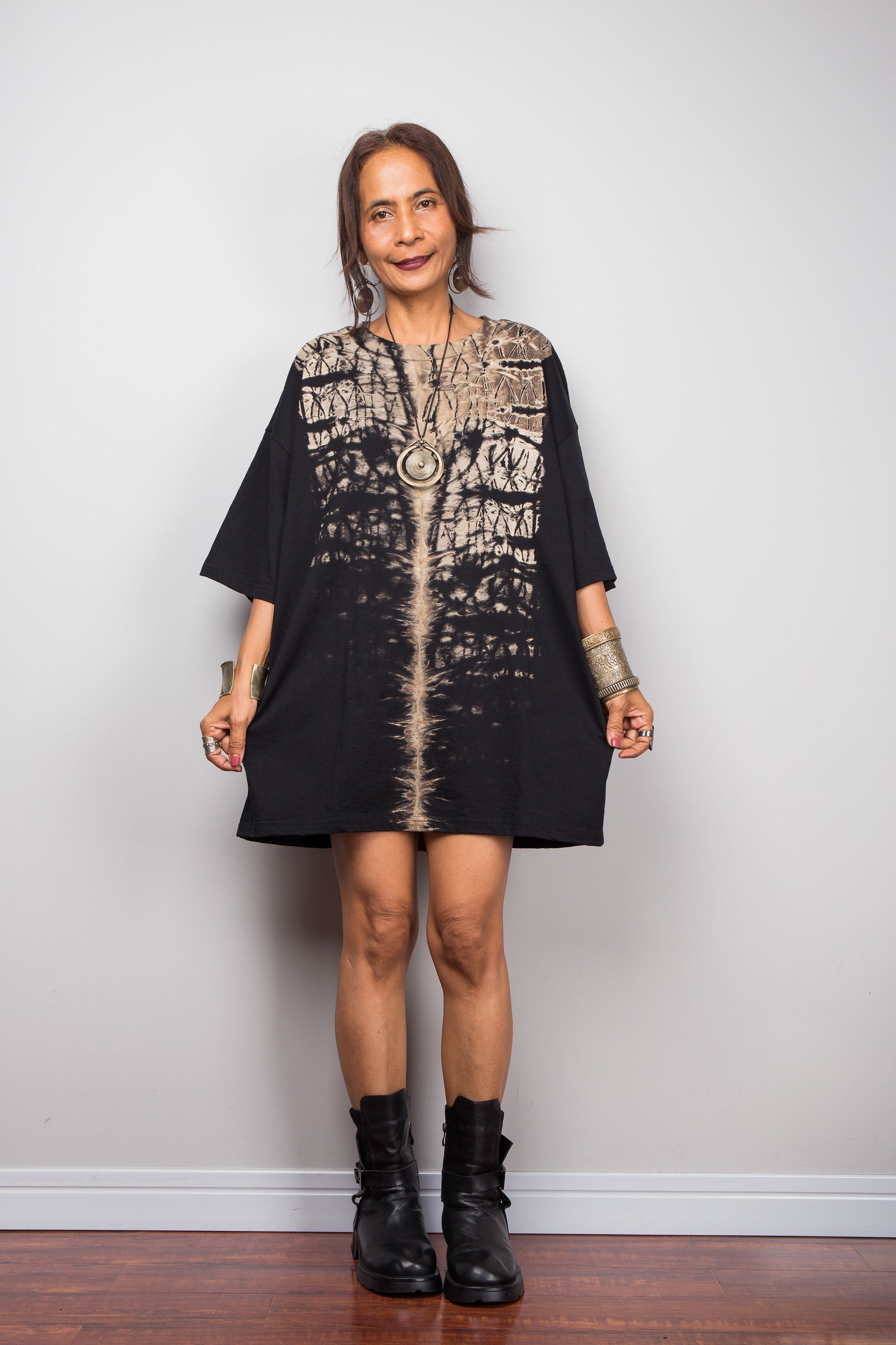 Front view of a petite woman styling Nuichan's oversized reverse tie-dye t-shirt dress with black boots, showcasing the loose boxy fit and vertical sand-colored starburst pattern