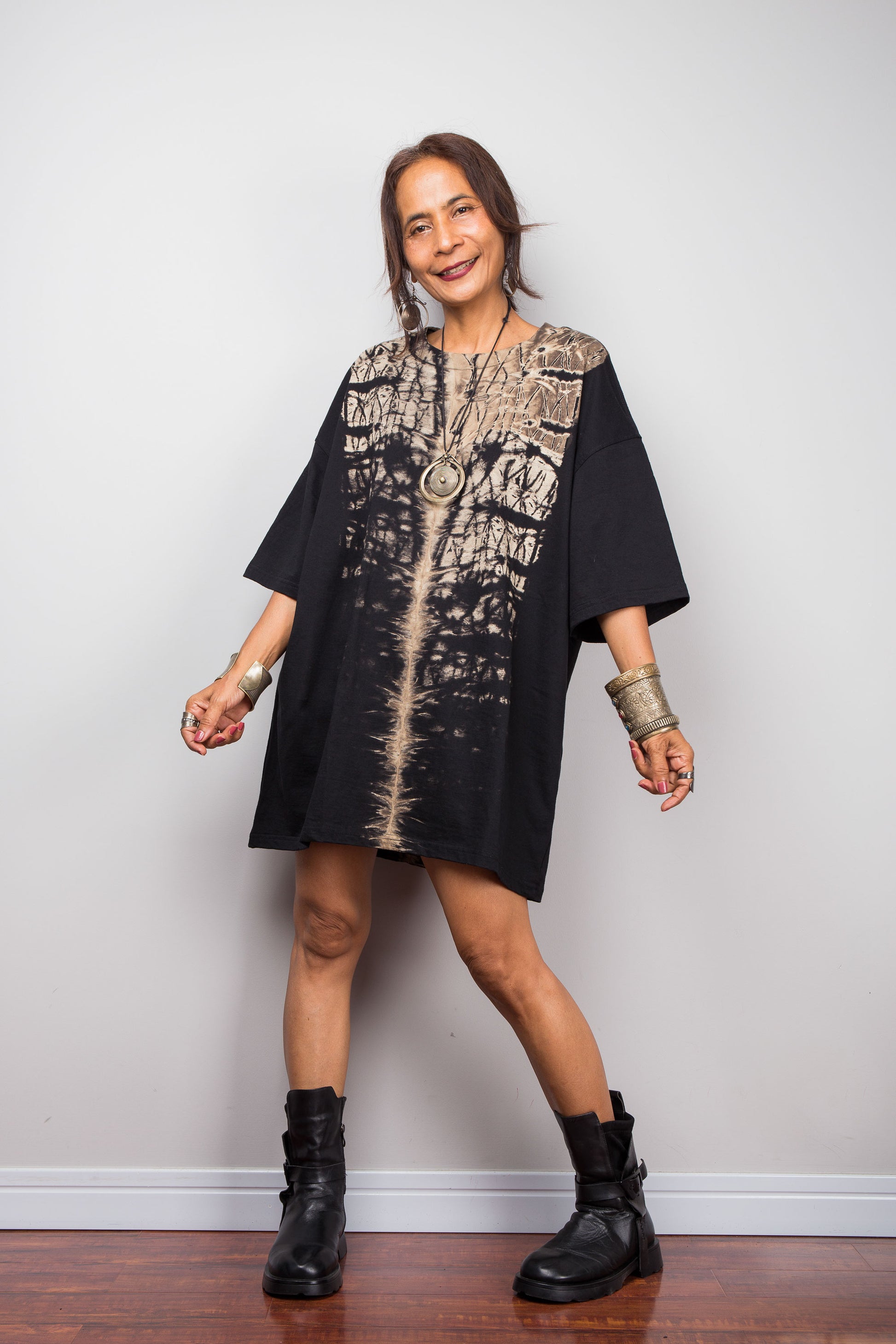 Front view of a woman styling Nuichan's oversized reverse tie-dye t-shirt dress with black boots, showcasing the loose boxy fit and vertical sand-colored starburst pattern