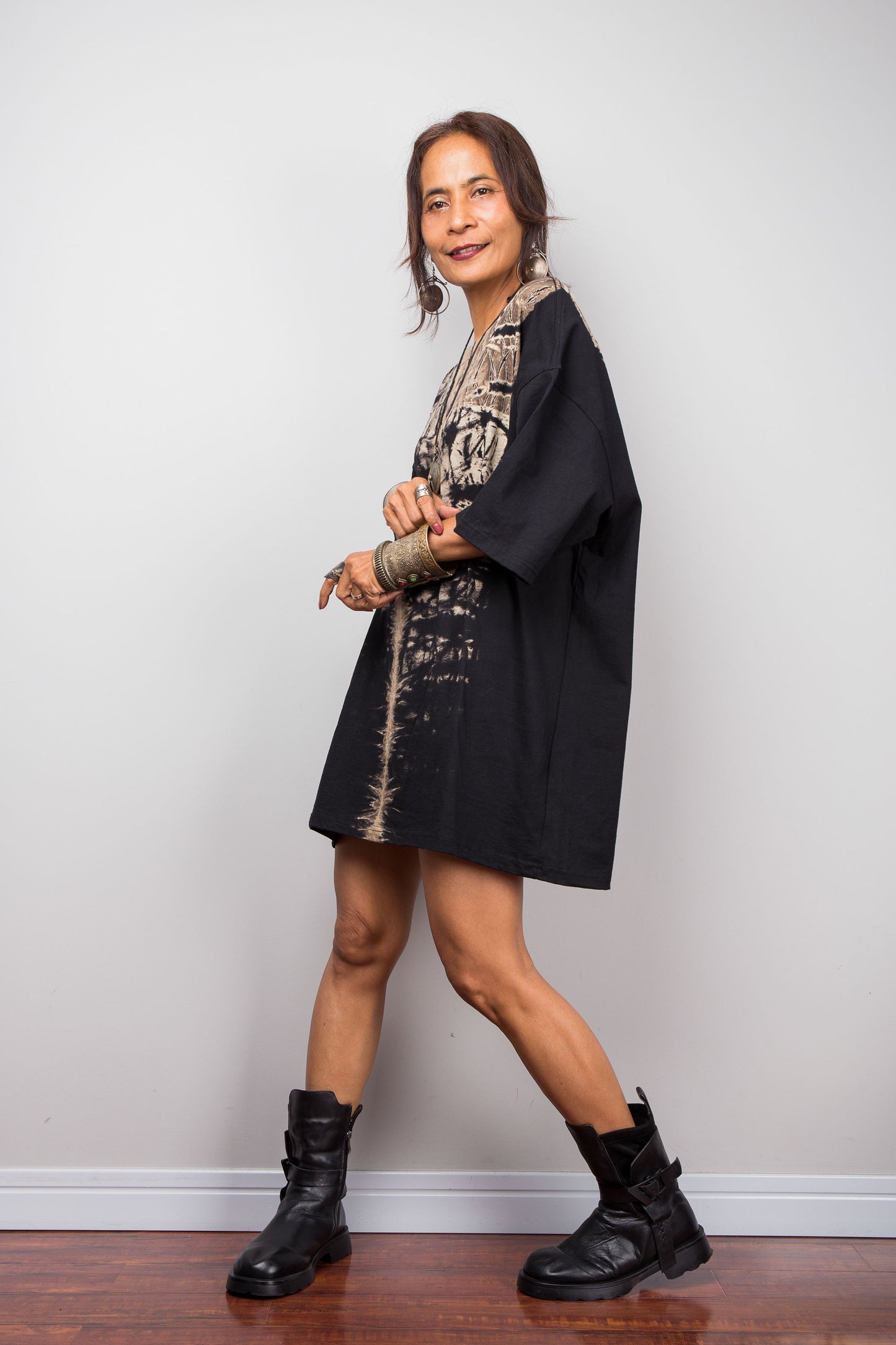 Side view of a model styling Nuichan's oversized reverse tie-dye t-shirt dress with black boots, showcasing the loose boxy fit and vertical sand-colored starburst pattern