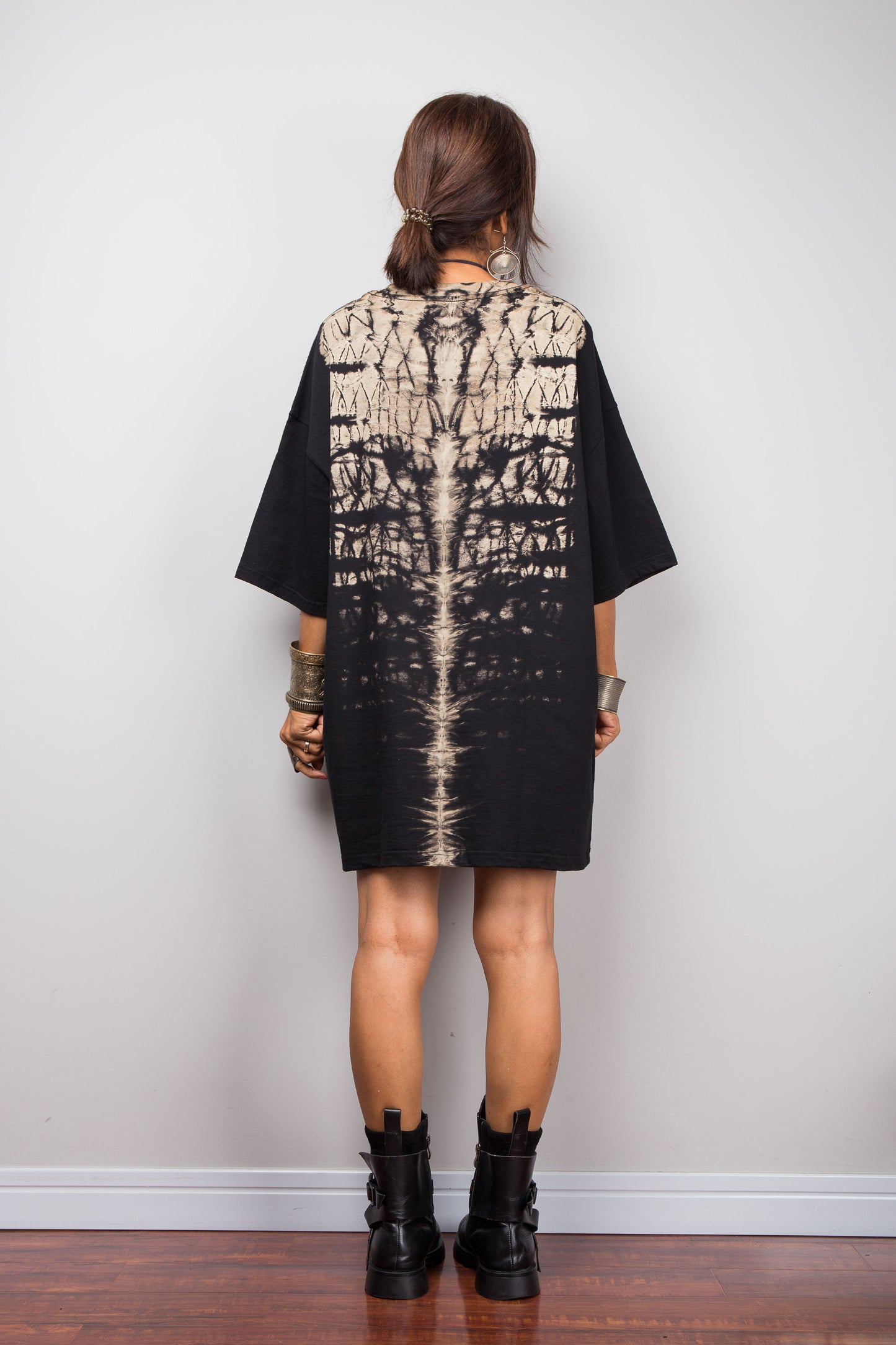 Back view of a model styling Nuichan's oversized reverse tie-dye t-shirt dress with black boots, showcasing the loose boxy fit and vertical sand-colored starburst pattern