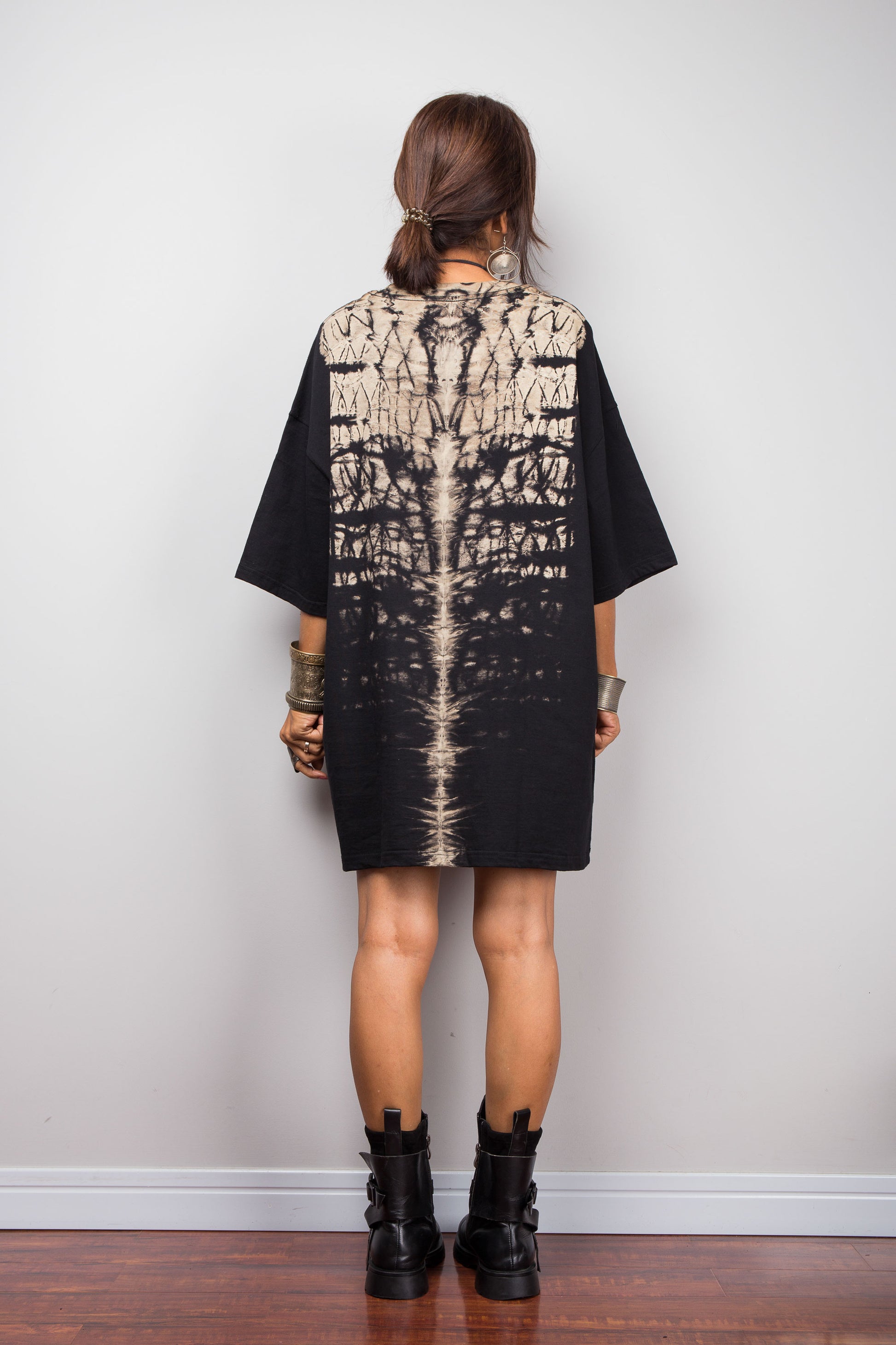 Back view of a model styling Nuichan's oversized reverse tie-dye t-shirt dress with black boots, showcasing the loose boxy fit and vertical sand-colored starburst pattern