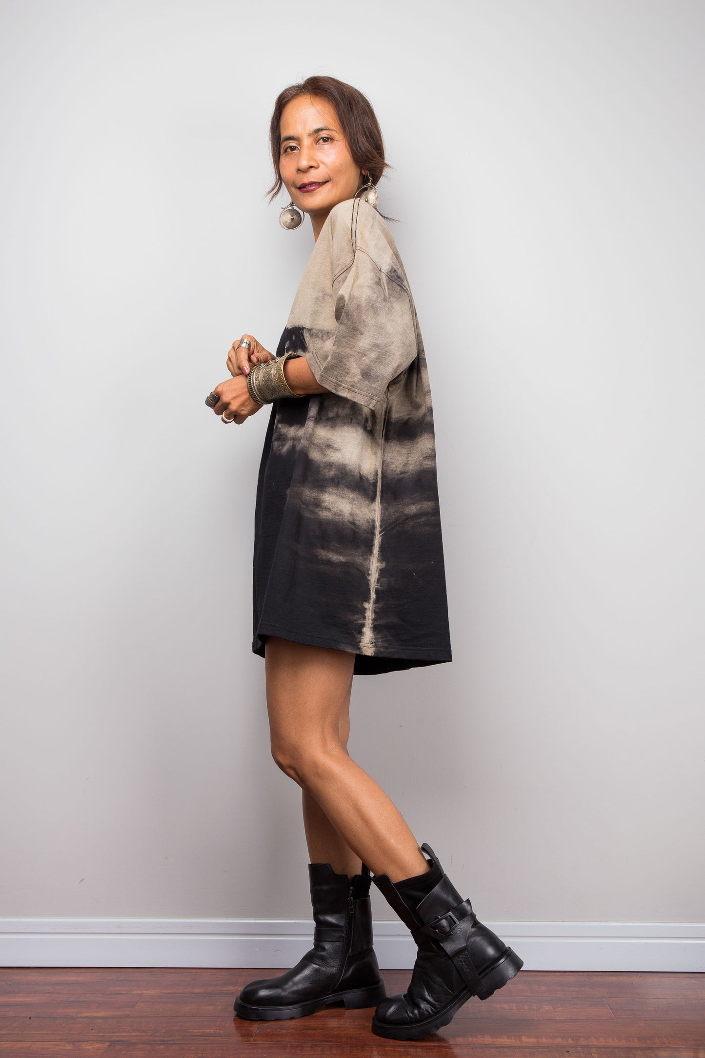 Side view of a petite female model styling Nuichan's oversized reverse tie-dye tee with black boots, showcasing the loose boxy fit and sand-colored pattern