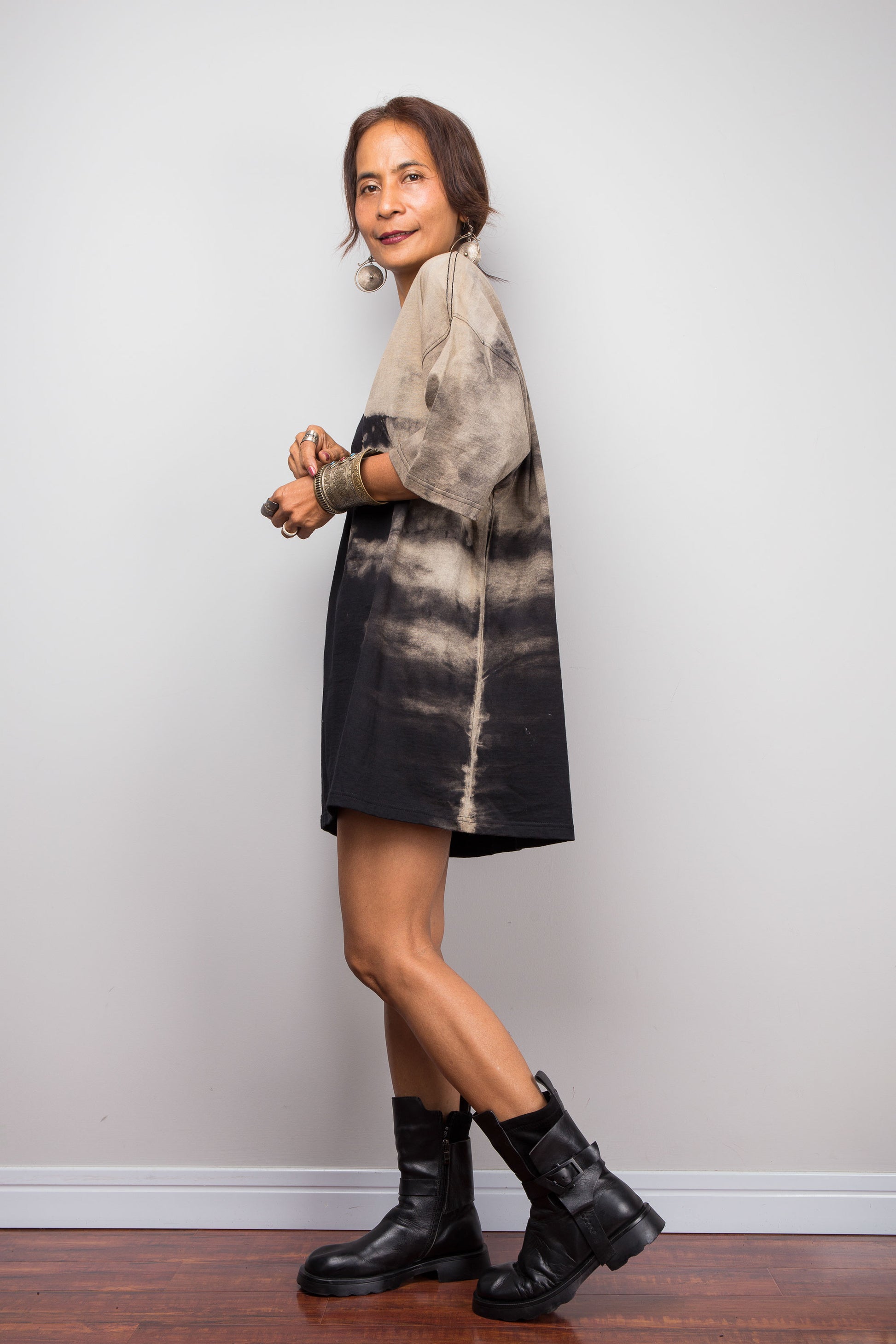 Side view of a petite female model styling Nuichan's oversized reverse tie-dye tee with black boots, showcasing the loose boxy fit and sand-colored pattern
