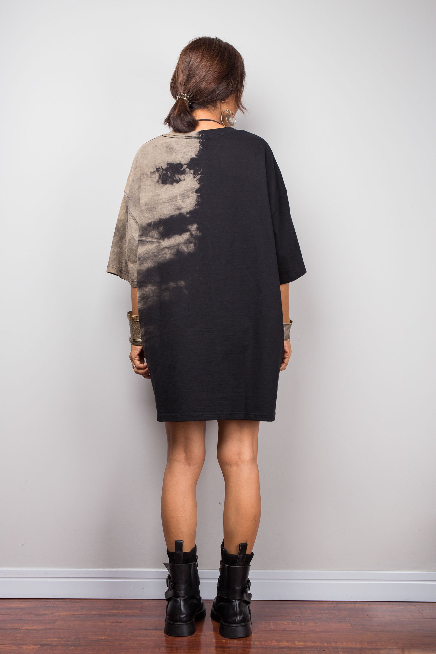 Rear view of a model styling Nuichan's oversized reverse tie-dye tee with black boots, showcasing the loose boxy fit and sand-colored pattern
