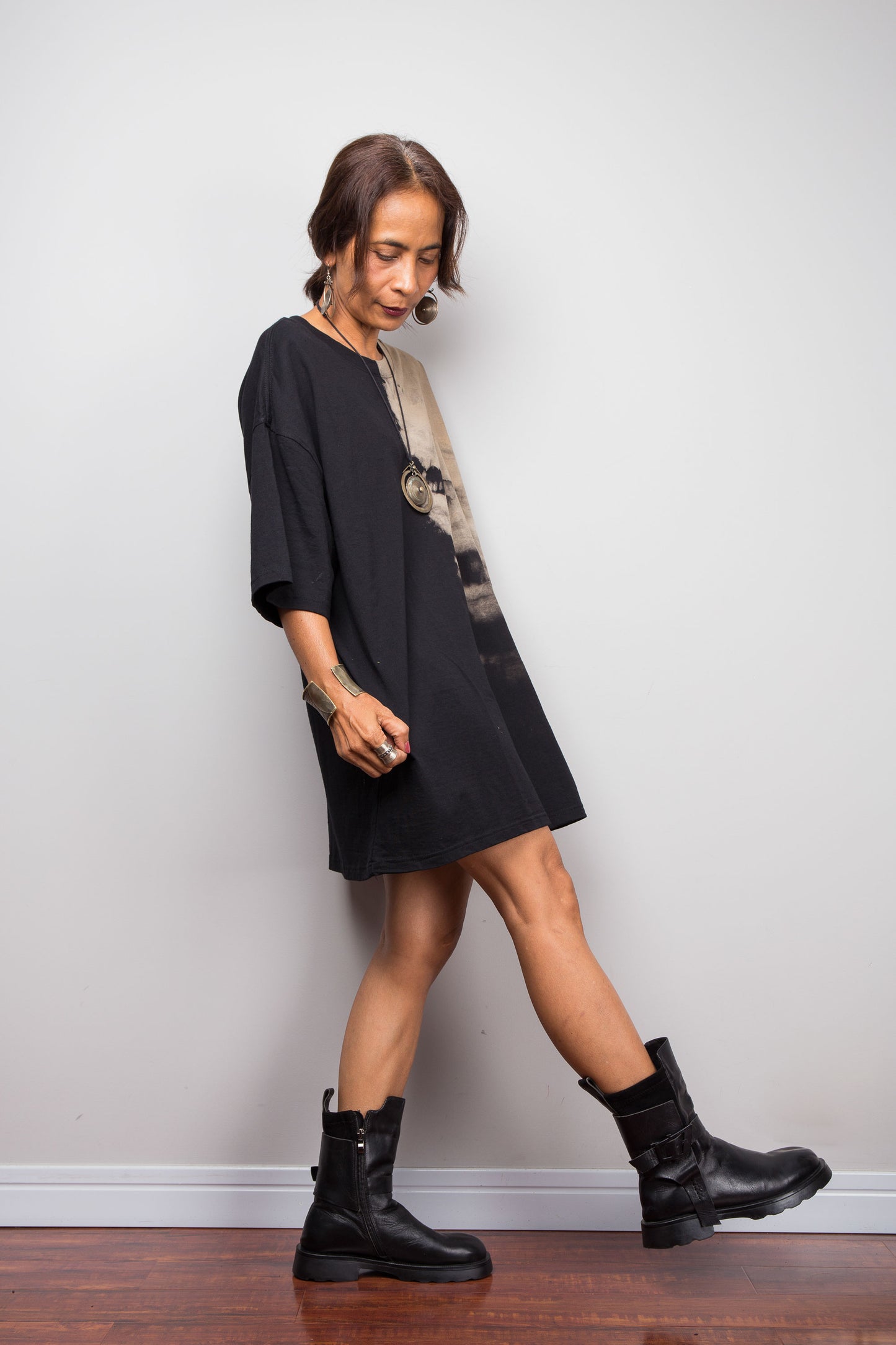 Woman wearing a black dress and black boots against a plain white wall.