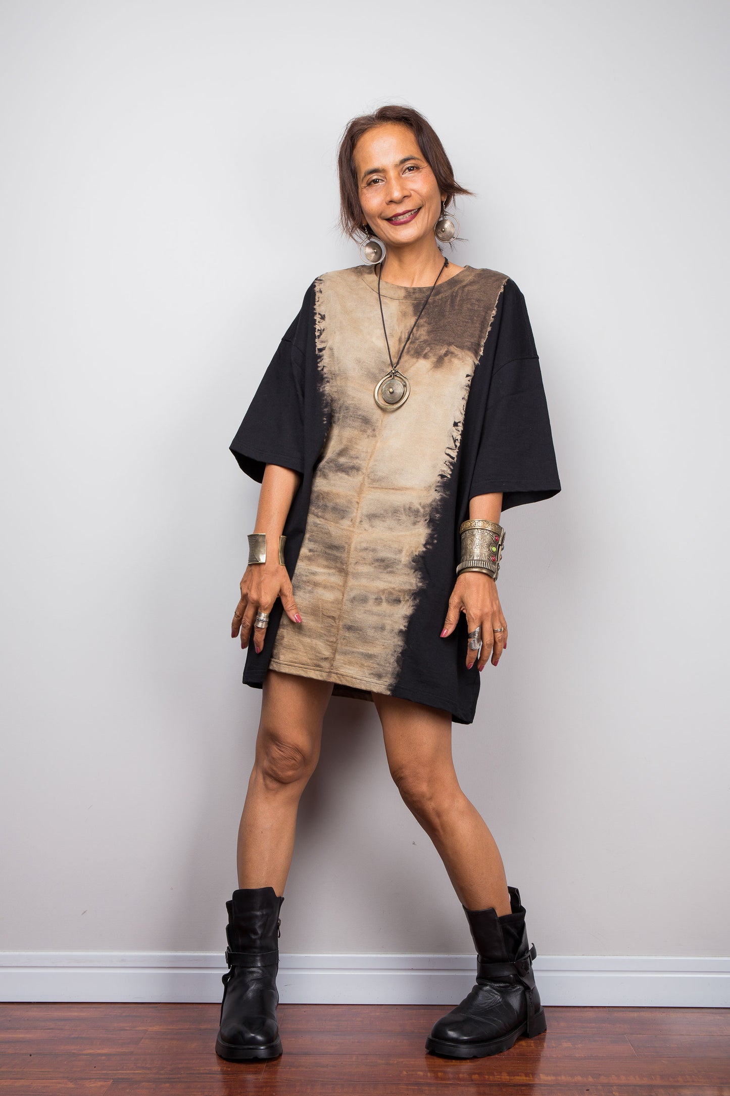 Front view of a petite woman styling Nuichan's oversized reverse tie dye t-shirt with black boots, showcasing the loose boxy fit and vertical sand-colored starburst pattern.