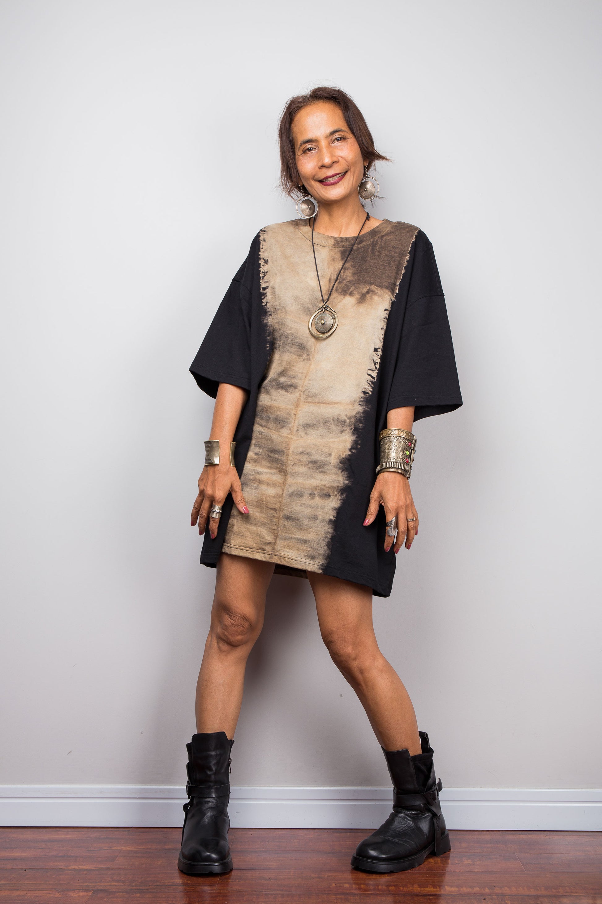 Front view of a petite woman styling Nuichan's oversized reverse tie dye t-shirt with black boots, showcasing the loose boxy fit and vertical sand-colored starburst pattern.