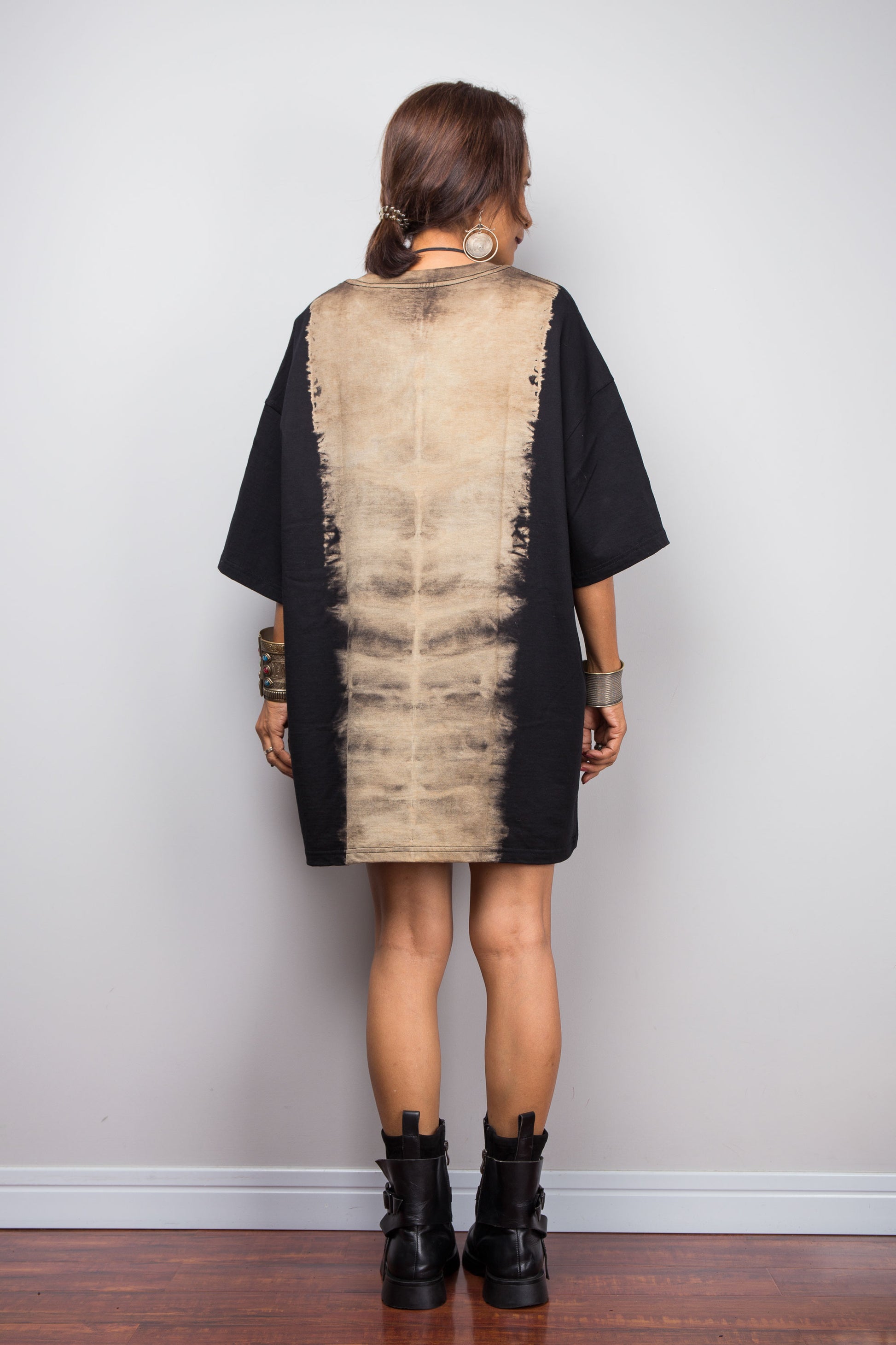 Back view of a model styling Nuichan's oversized reverse tie dye t-shirt with black boots, showcasing the loose boxy fit and vertical sand-colored starburst pattern.