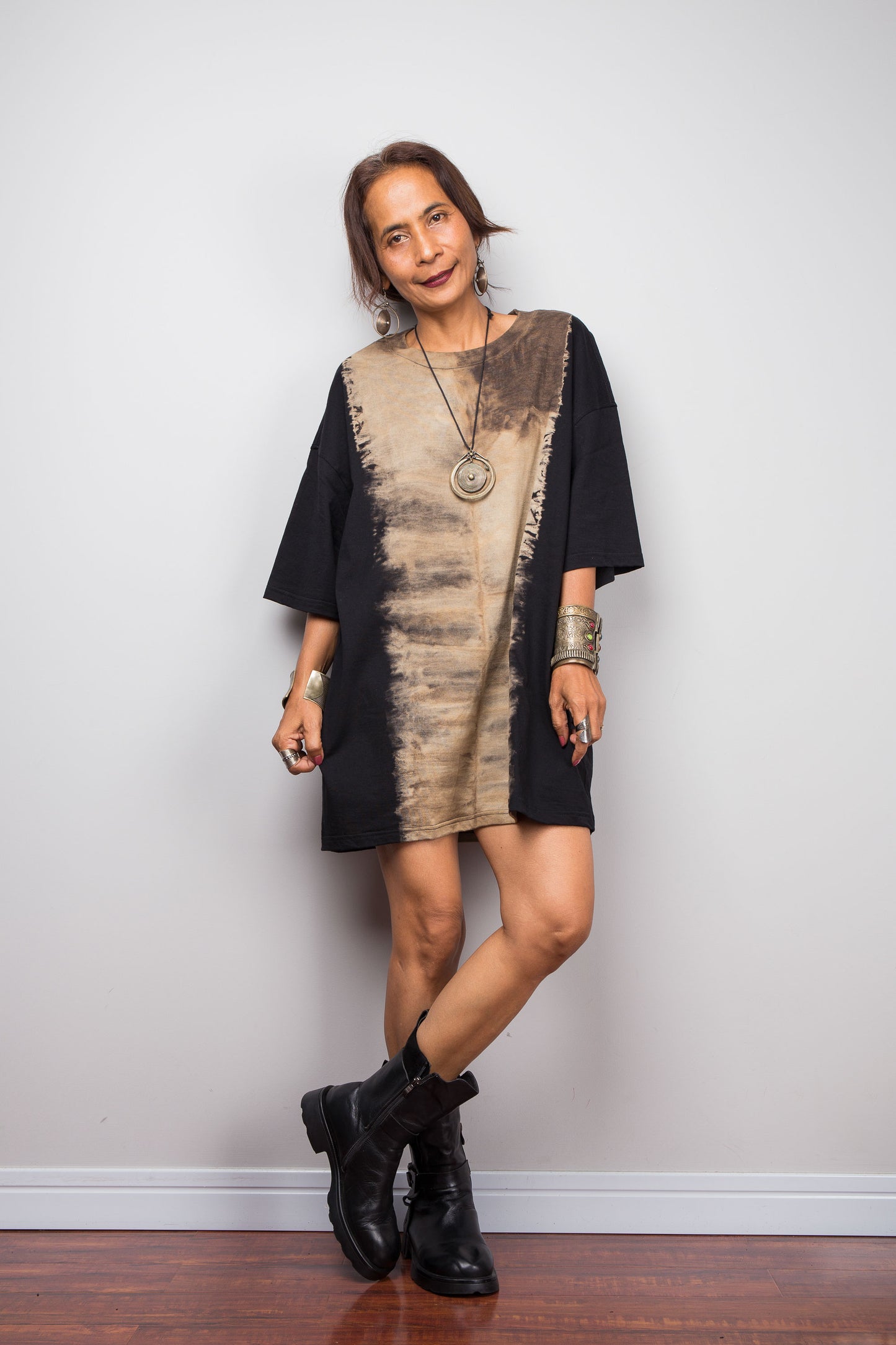 Front view of a petite model styling Nuichan's oversized reverse tie dye t-shirt with black boots, showcasing the loose boxy fit and vertical sand-colored starburst pattern.