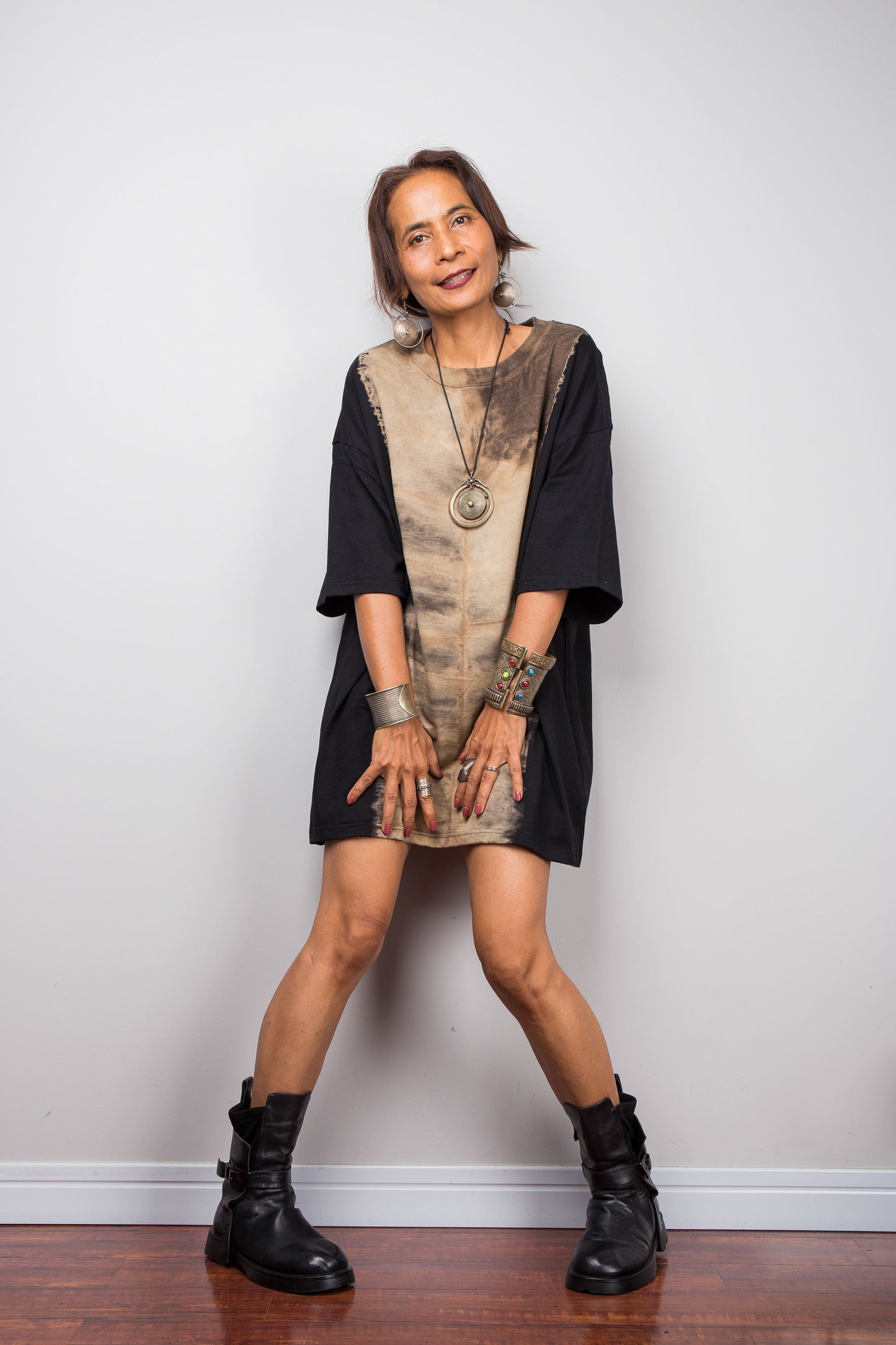 Front view of a petite female model styling Nuichan's oversized reverse tie dye t-shirt with black boots, showcasing the loose boxy fit and vertical sand-colored starburst pattern.