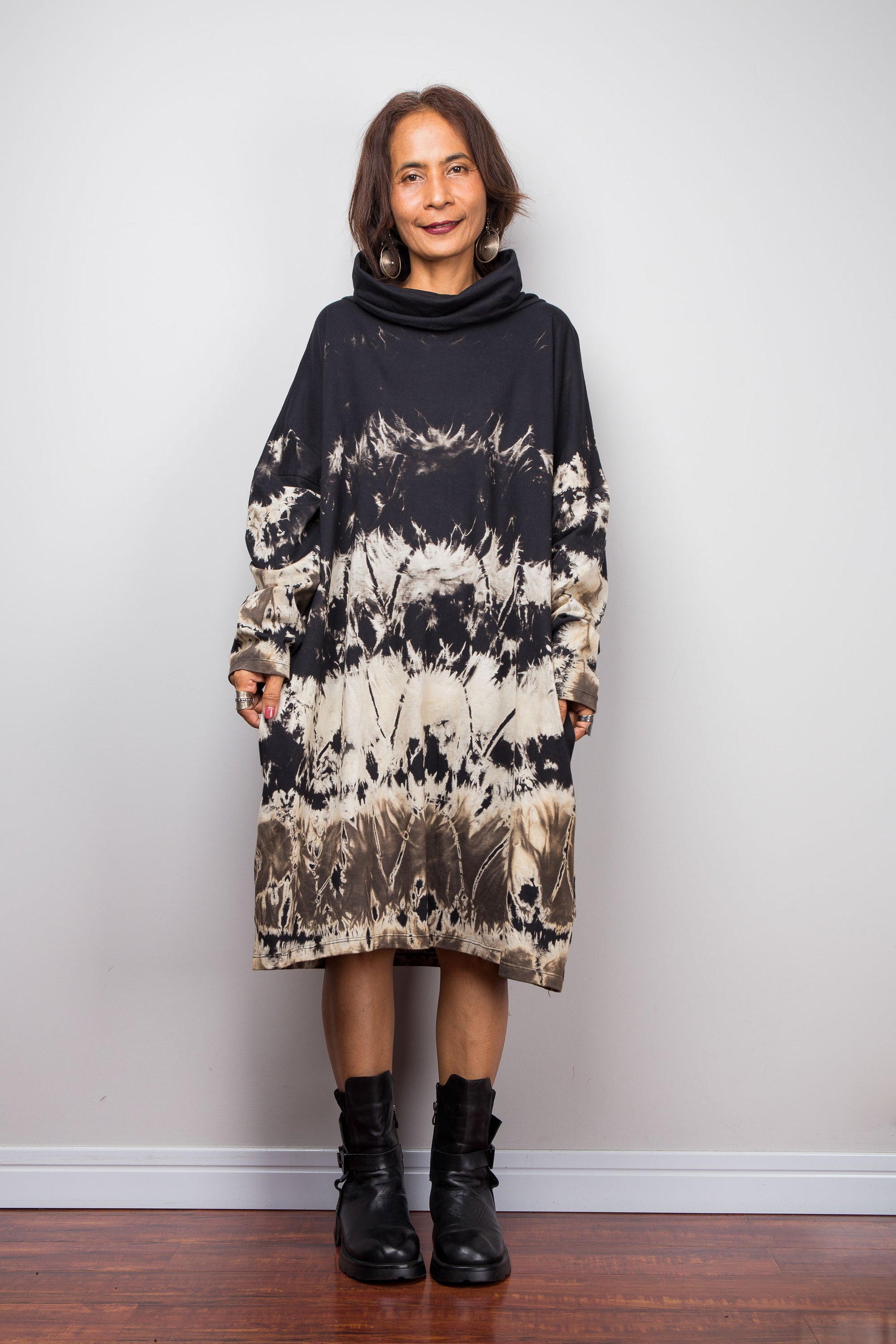 Petite women wearing an Oversized Nuichan reverse tie-dye tunic dress featuring a funnel cowl neck and abstract sand and black patterns.  Frontal view with arms next to the body