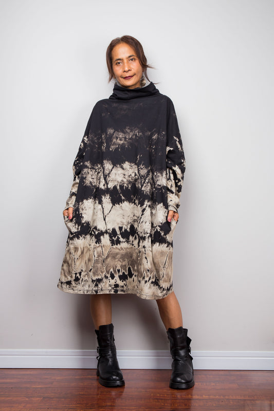 Full front view of a model wearing Nuichan's oversized reverse tie dye tunic dress with a high funnel cowl neck, pockets and horizontal abstract sand-colored patterns.