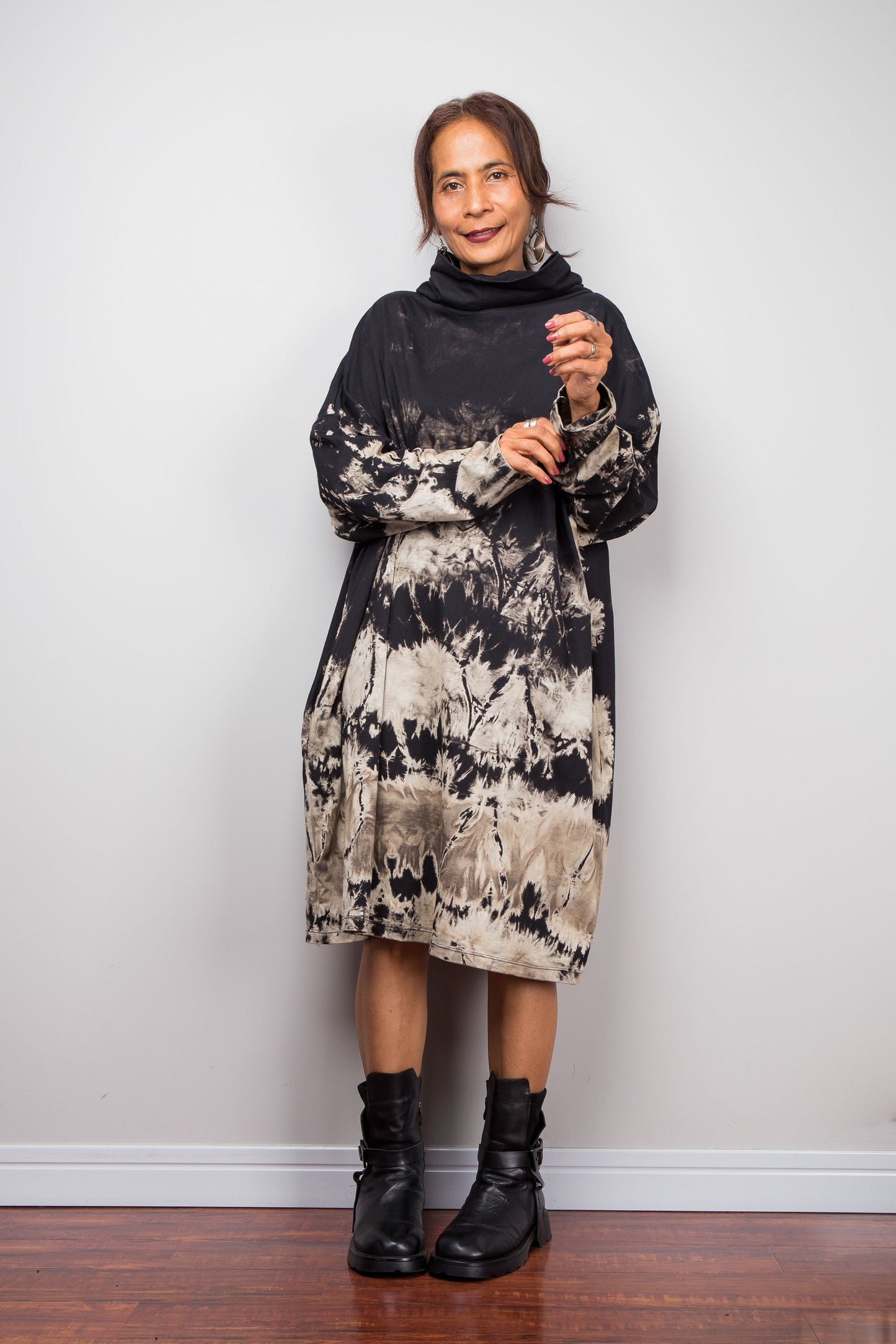 Full front view of a model wearing Nuichan's oversized reverse tie-dye tunic dress with a high funnel cowl neck, long sleeves, pockets and horizontal abstract sand-colored patterns.
