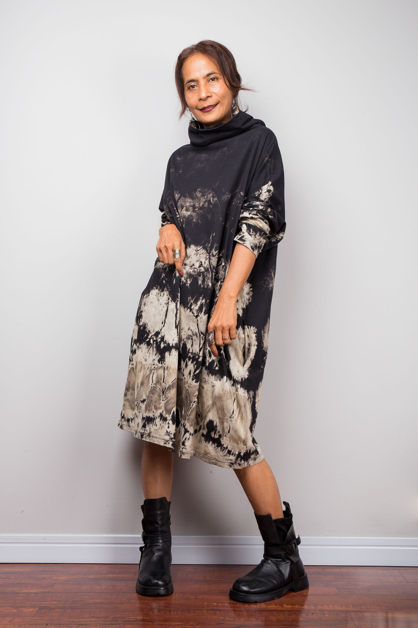 Full front view of a model wearing Nuichan's oversized reverse tie-dye tunic dress with a high funnel cowl neck and horizontal abstract sand-colored patterns and rolled up sleeves.