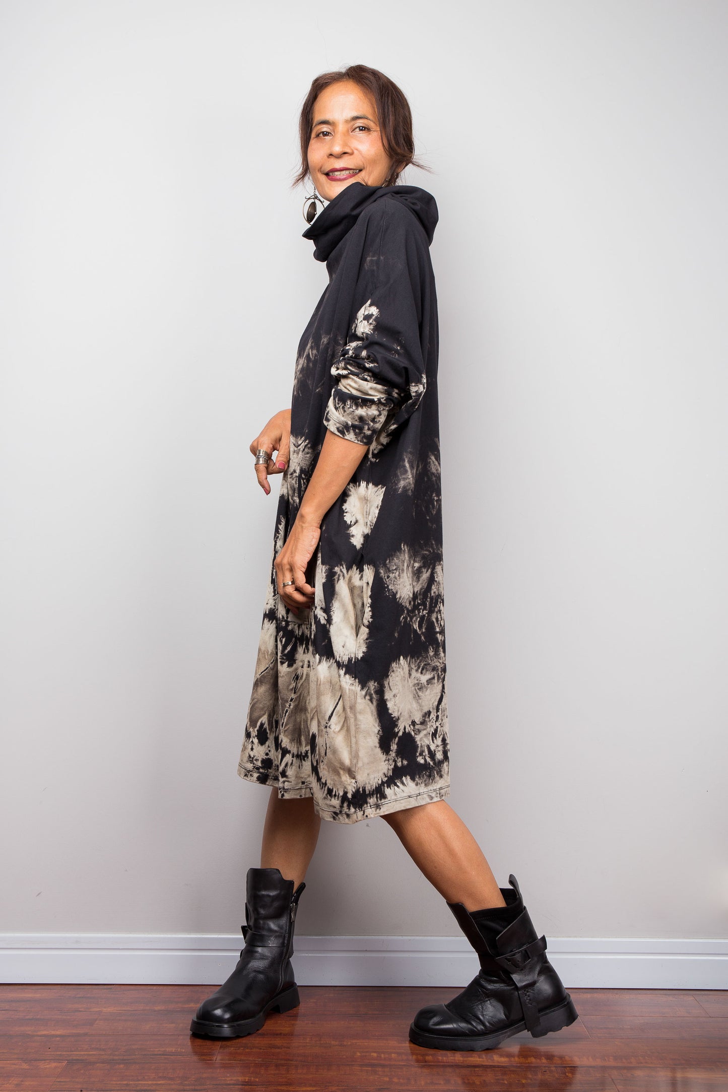 Side view of a model wearing Nuichan's oversized reverse tie dye tunic dress with a high funnel cowl neck and horizontal abstract sand-colored patterns.