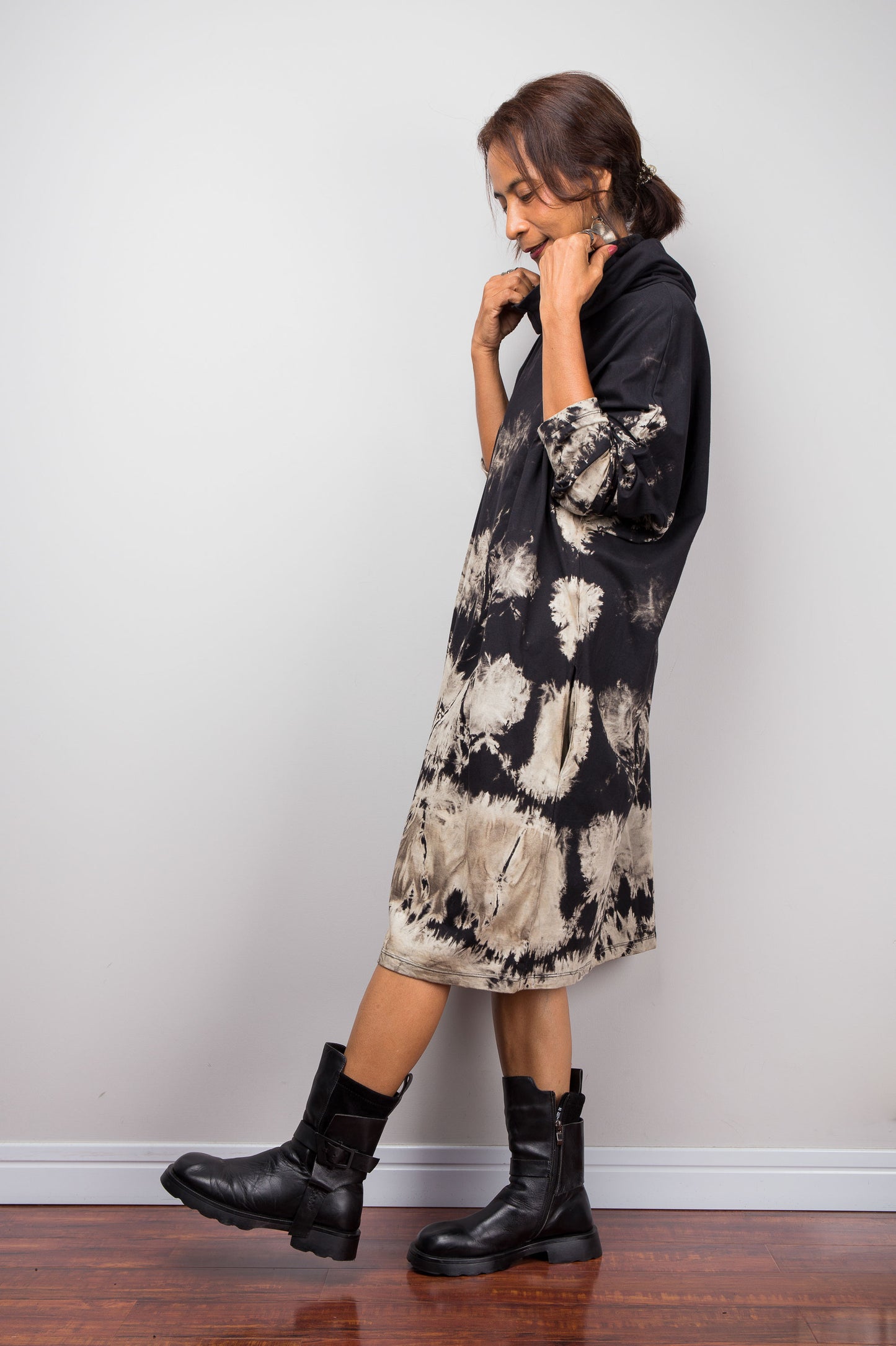 Full side view of a model wearing Nuichan's oversized reverse tie-dye tunic dress with a high funnel cowl neck and horizontal abstract sand-colored patterns.