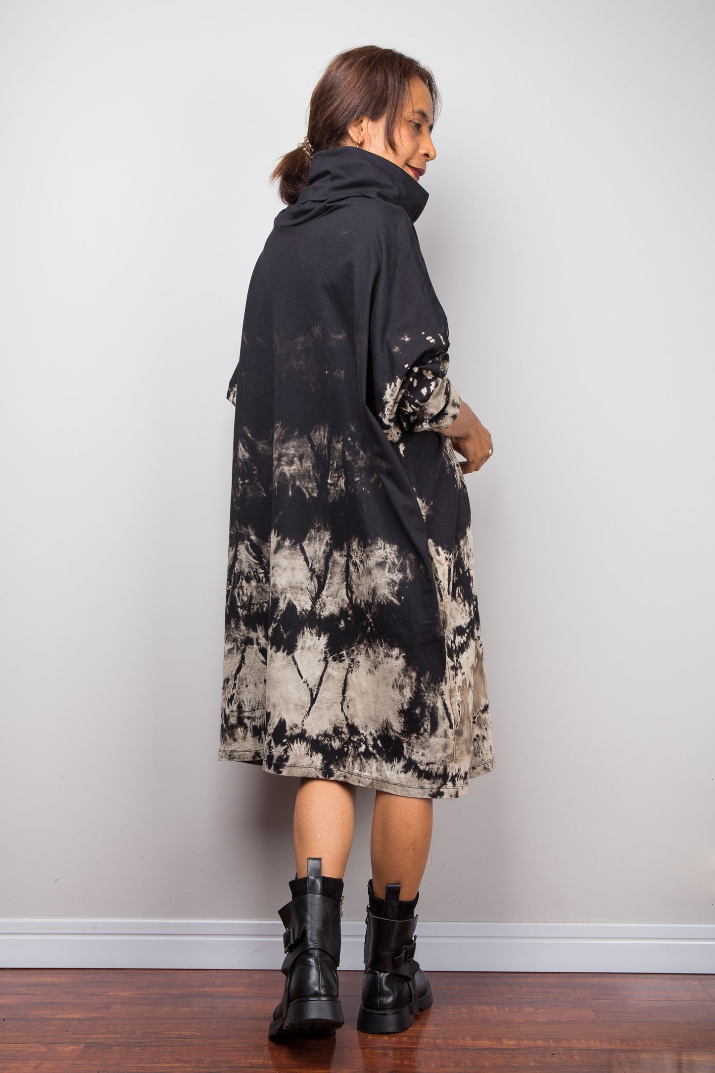 Back view of a model wearing Nuichan's oversized reverse tie-dye tunic dress with a high funnel cowl neck and horizontal abstract sand-colored patterns.