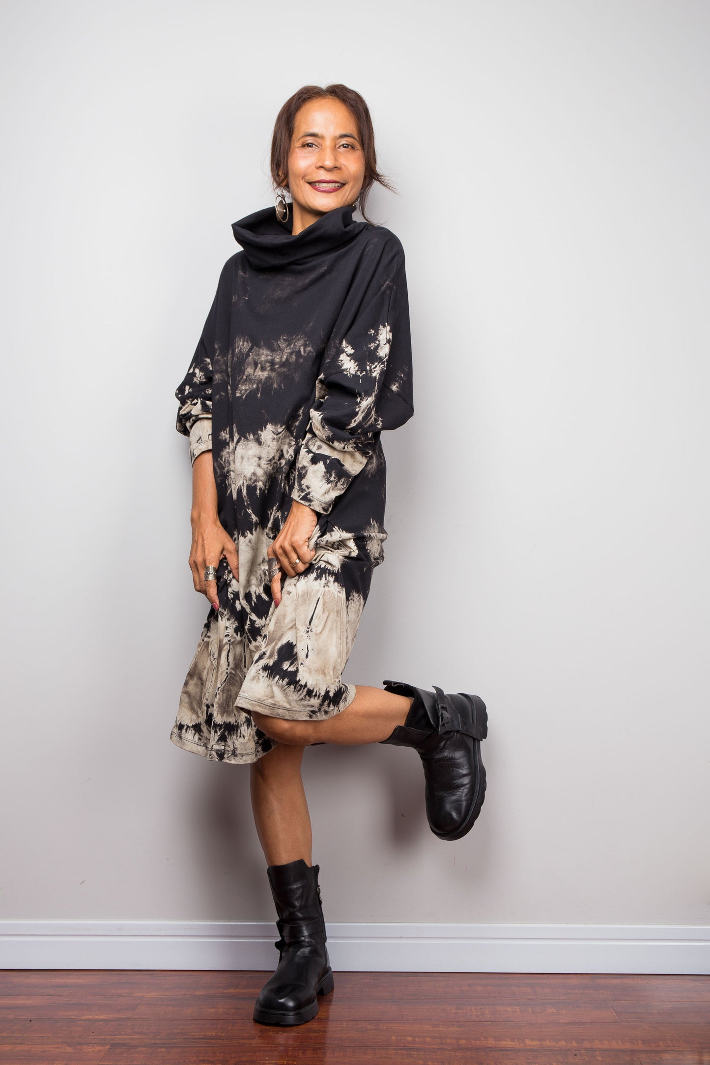 Full front view of a model wearing Nuichan's oversized reverse tie dye tunic dress with a high funnel cowl neck and horizontal abstract sand-colored patterns.