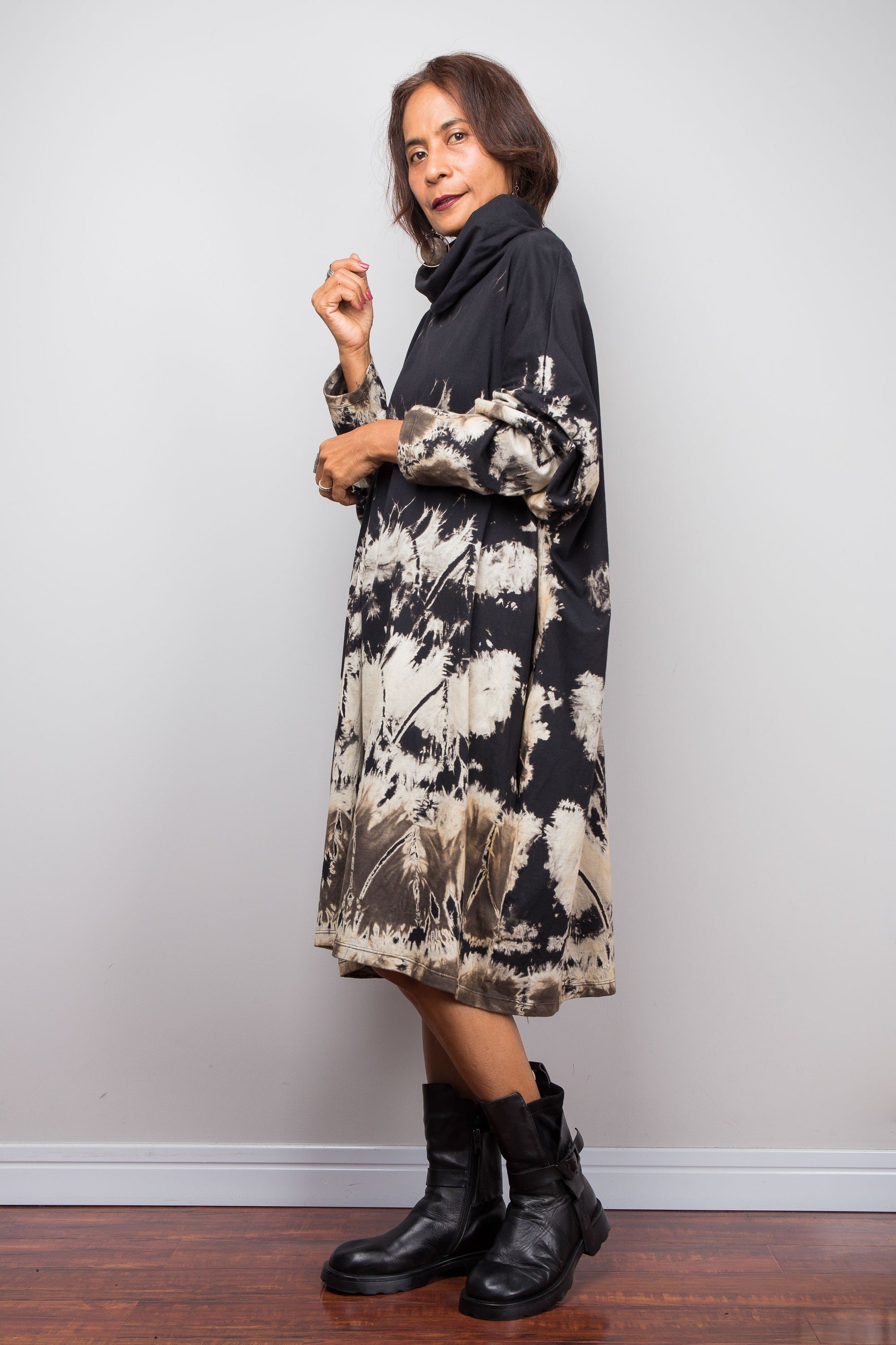 Petite women wearing an Oversized Nuichan reverse tie-dye tunic dress featuring a funnel cowl neck and abstract sand and black patterns.  Side on view
