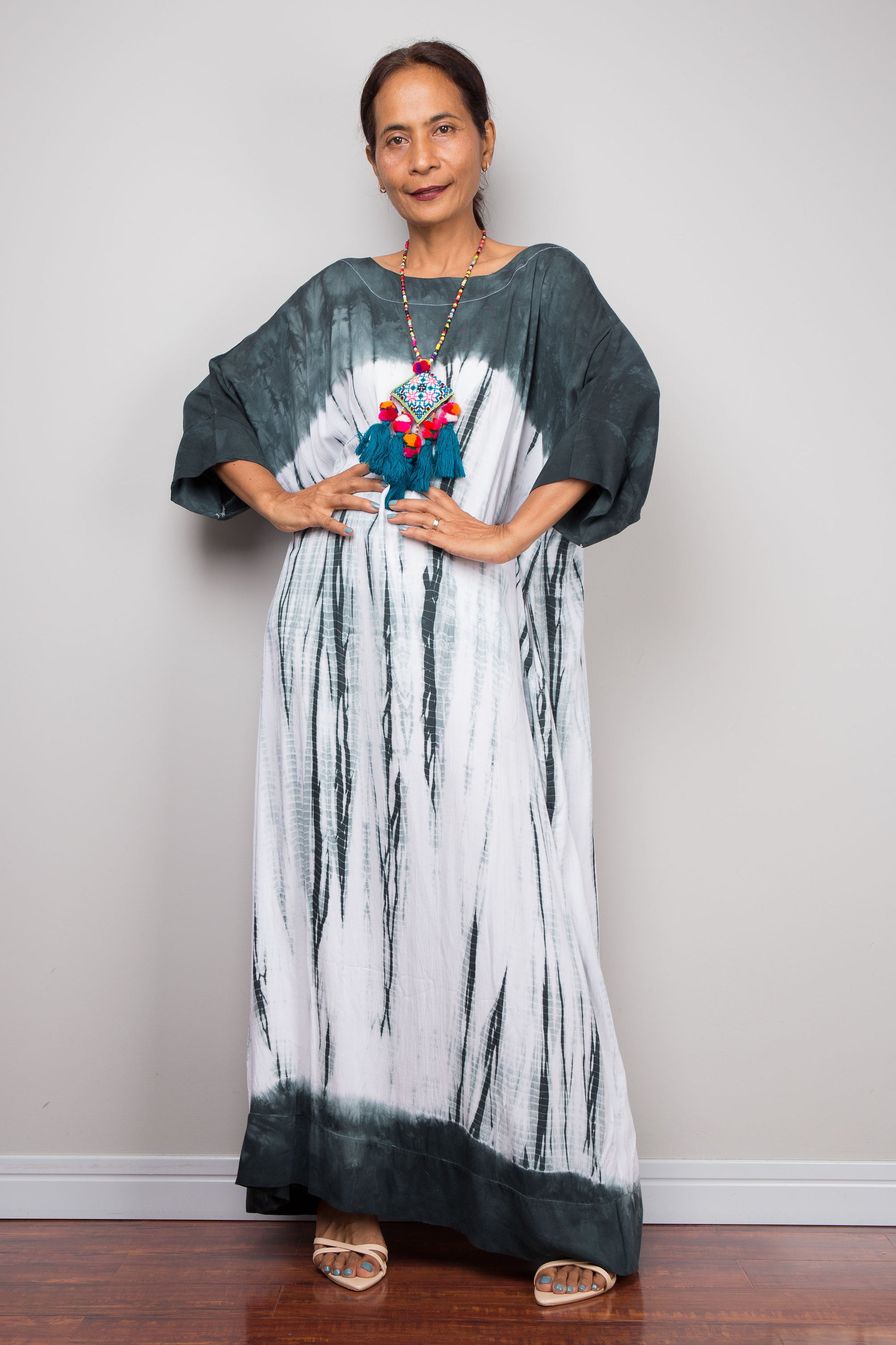 A woman wearing a loose-fitting, floor-length monochrome Shibori tie dye maxi kaftan dress from nuichan.com, featuring a charcoal-grey yoke and white abstract drip-effect skirt.