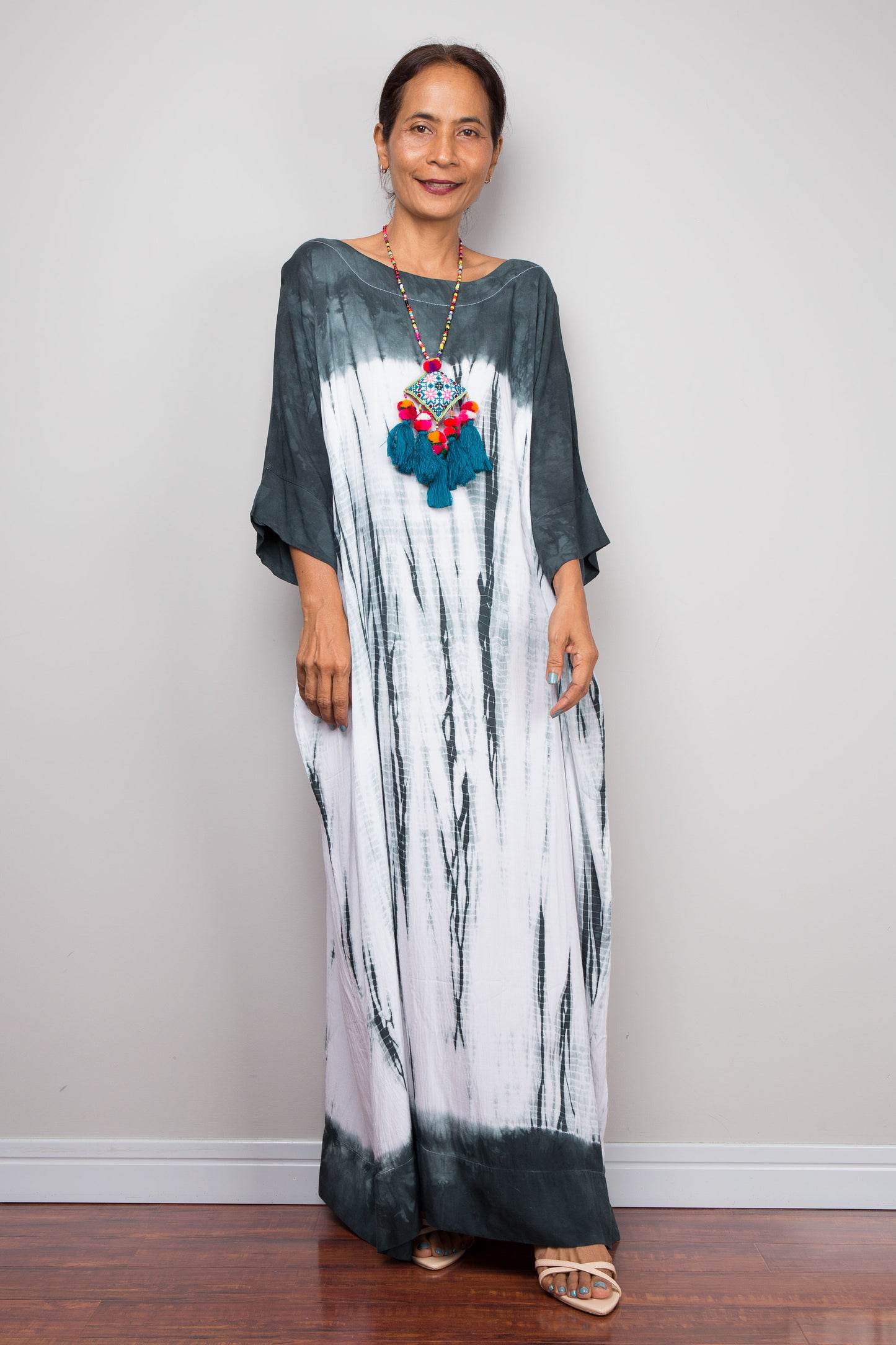 Woman wearing a long, patterned tie dye shibori dress against a plain background