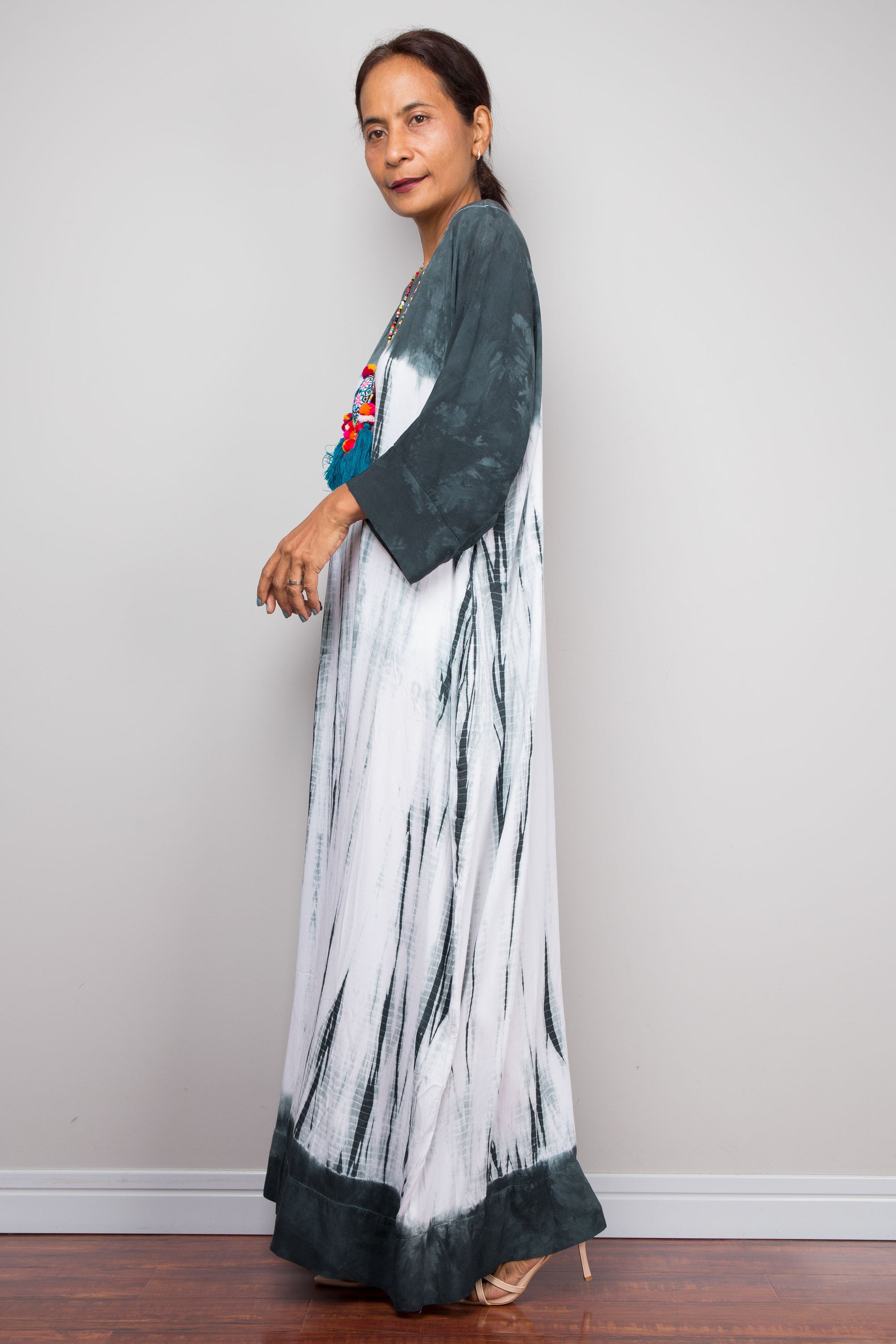 Woman wearing a long, patterned shibori tie dye maxi dress with a plain background