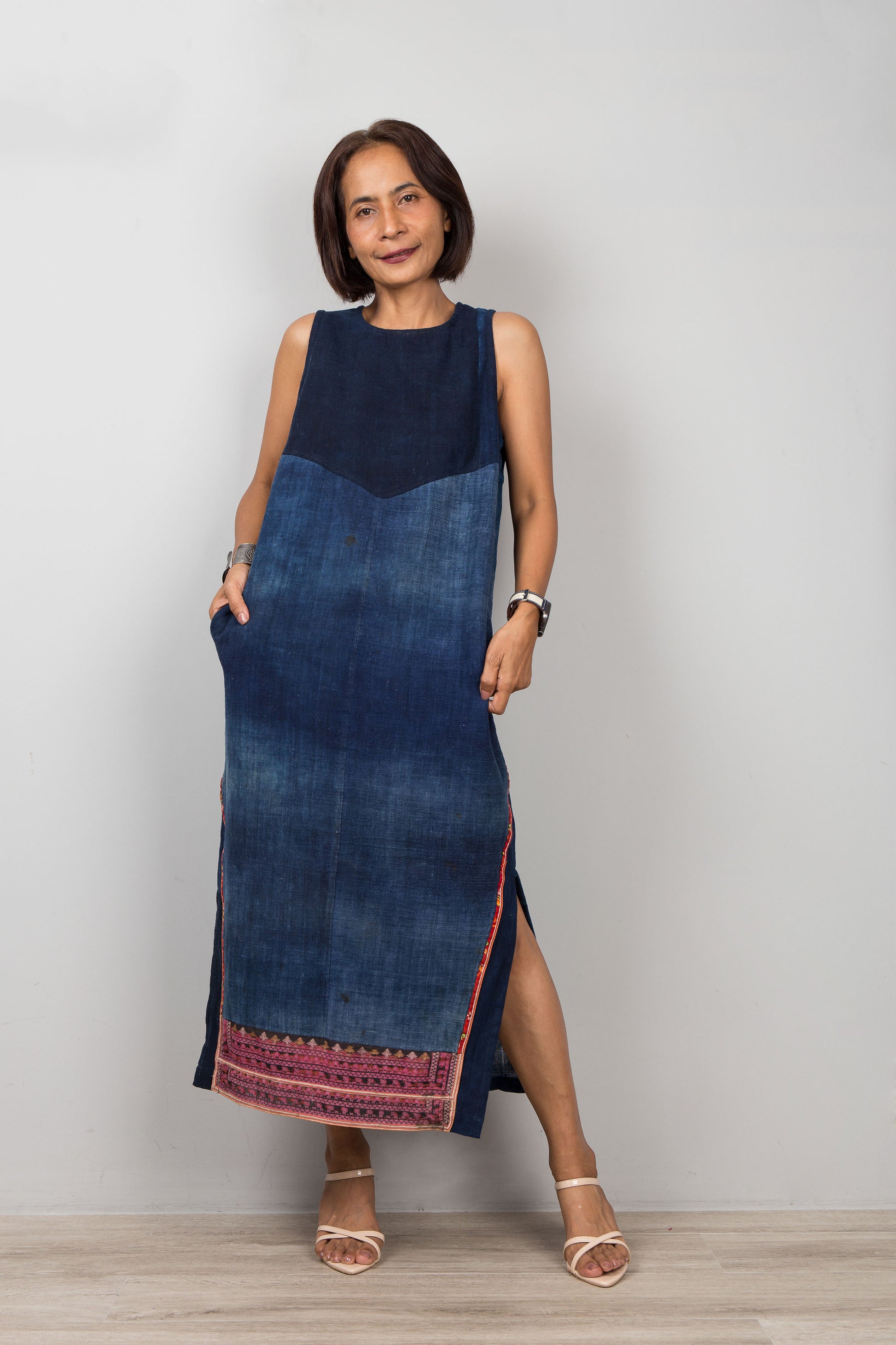 Nuichan wearing a blue cotton dress with embroidery, pockets and a slit on a plain background