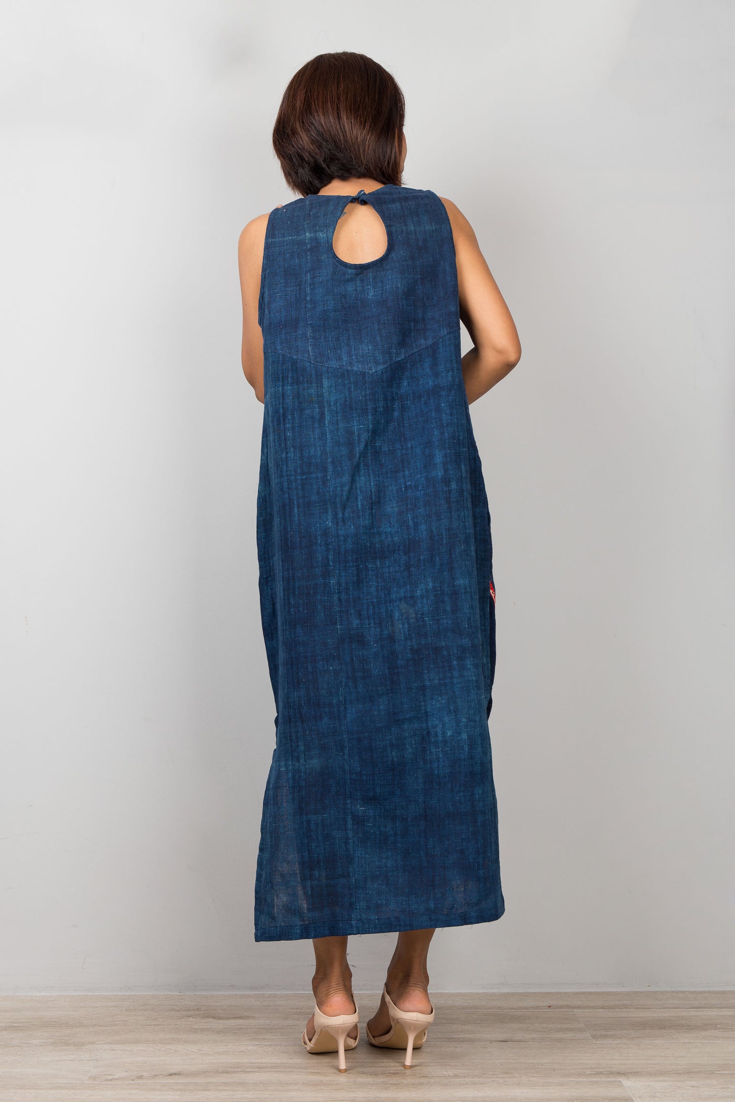 Woman wearing a blue cotton dress with embroidery, pockets and a slit on a plain background
