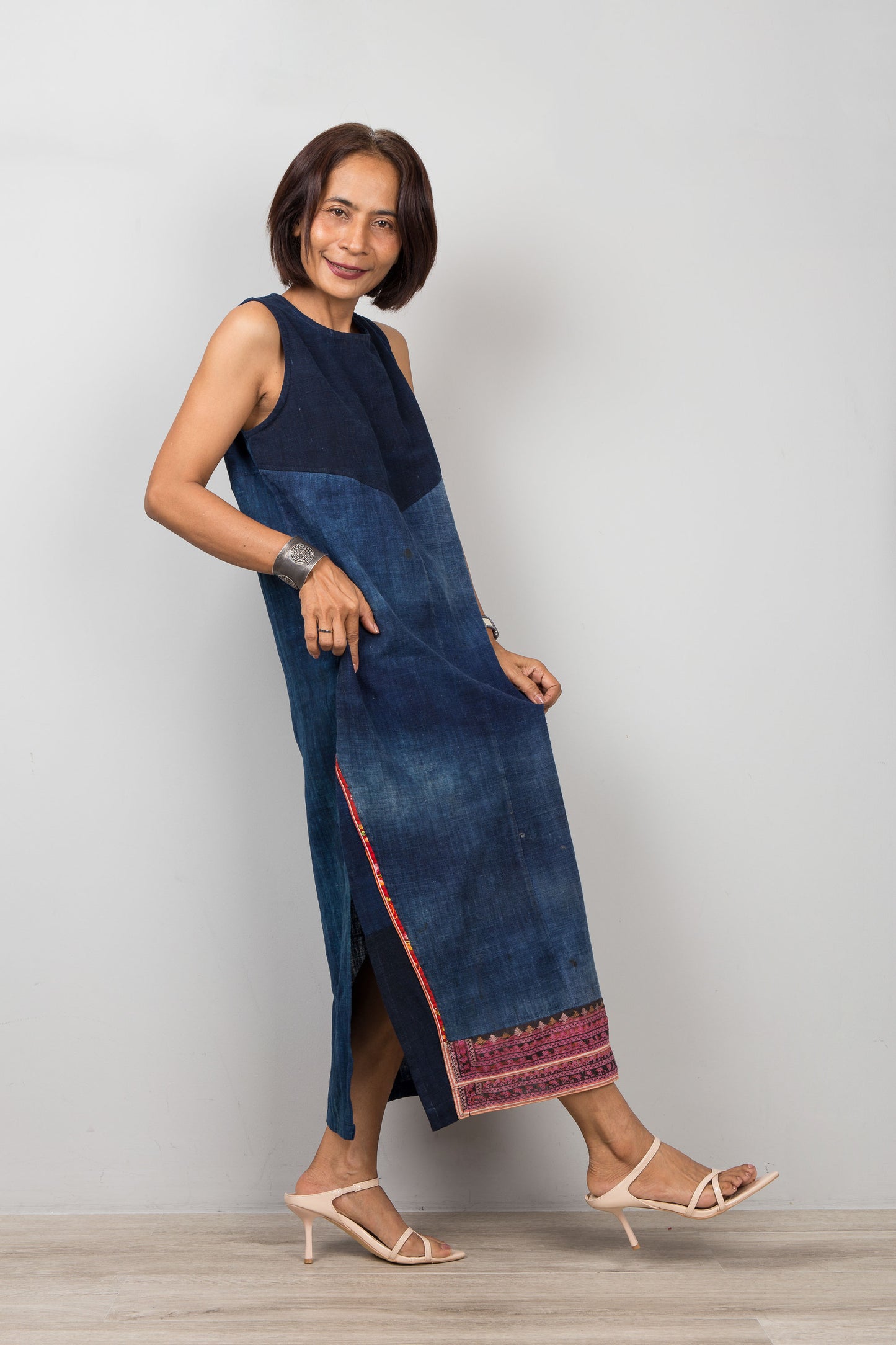 Petite Woman wearing a blue cotton dress with embroidery, pockets and a slit on a plain background