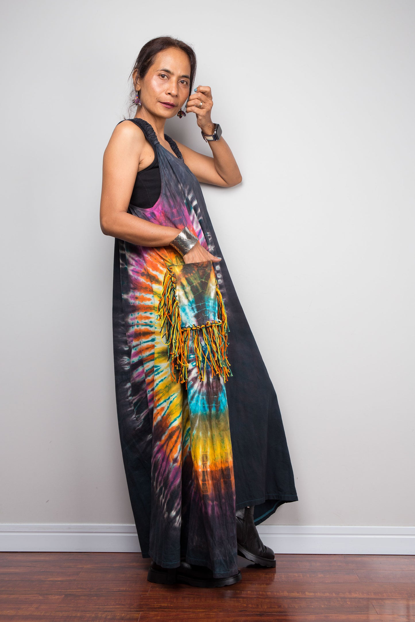 Side view of a model wearing the Nuichan sleeveless tie-dye boho maxi dress, showing the scoop neckline, flowing A-line silhouette, and multicolour yarn fringe patch pocket on the hip.