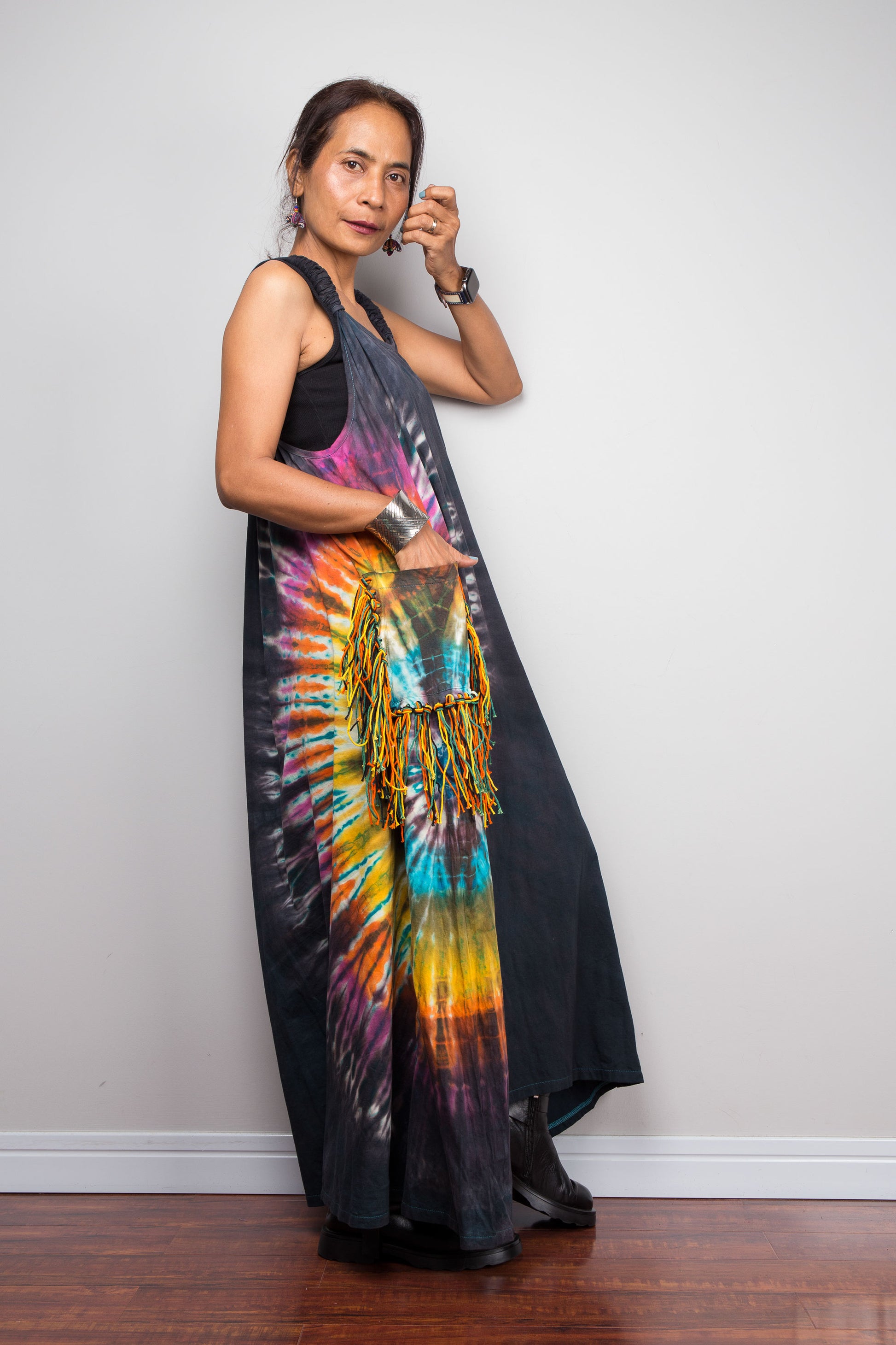 Side view of a model wearing the Nuichan sleeveless tie-dye boho maxi dress, showing the scoop neckline, flowing A-line silhouette, and multicolour yarn fringe patch pocket on the hip.
