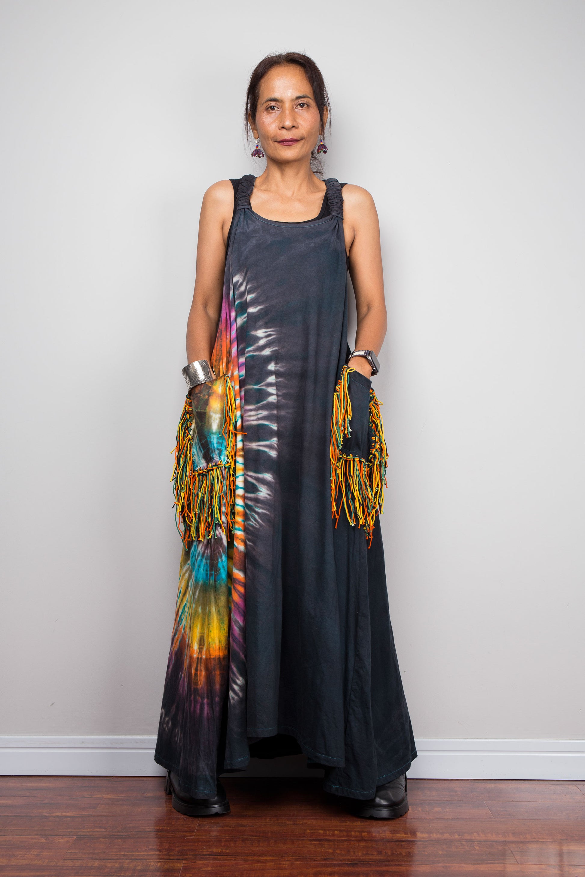 Front-facing view of a model wearing the Nuichan sleeveless tie dye boho maxi dress, showing the scoop neckline, flowing A-line silhouette, and multicolour yarn fringe patch pockets.