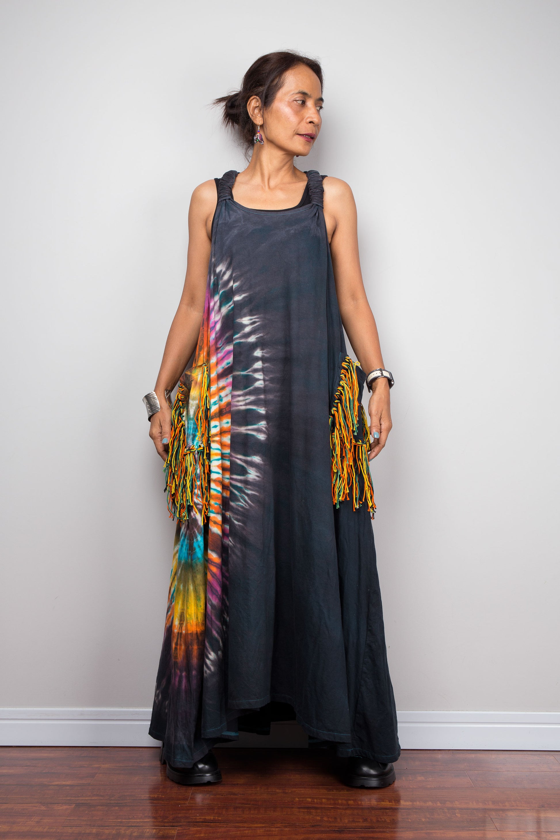 Front view of a petite model wearing the Nuichan sleeveless tie-dye boho maxi dress, showing the scoop neckline, flowing A-line silhouette, and multicolor yarn fringe patch pockets on both hips.