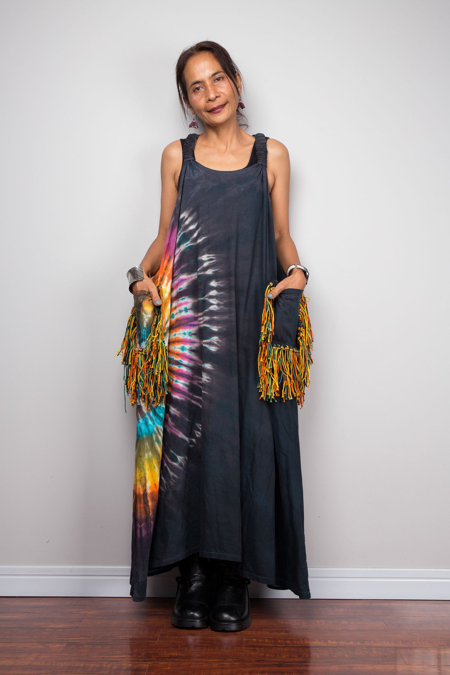 Front-facing view of a model wearing the Nuichan sleeveless tie-dye boho maxi dress, showing the scoop neckline, flowing A-line silhouette, and with both hands in the  multicolour yarn fringe patch pockets.